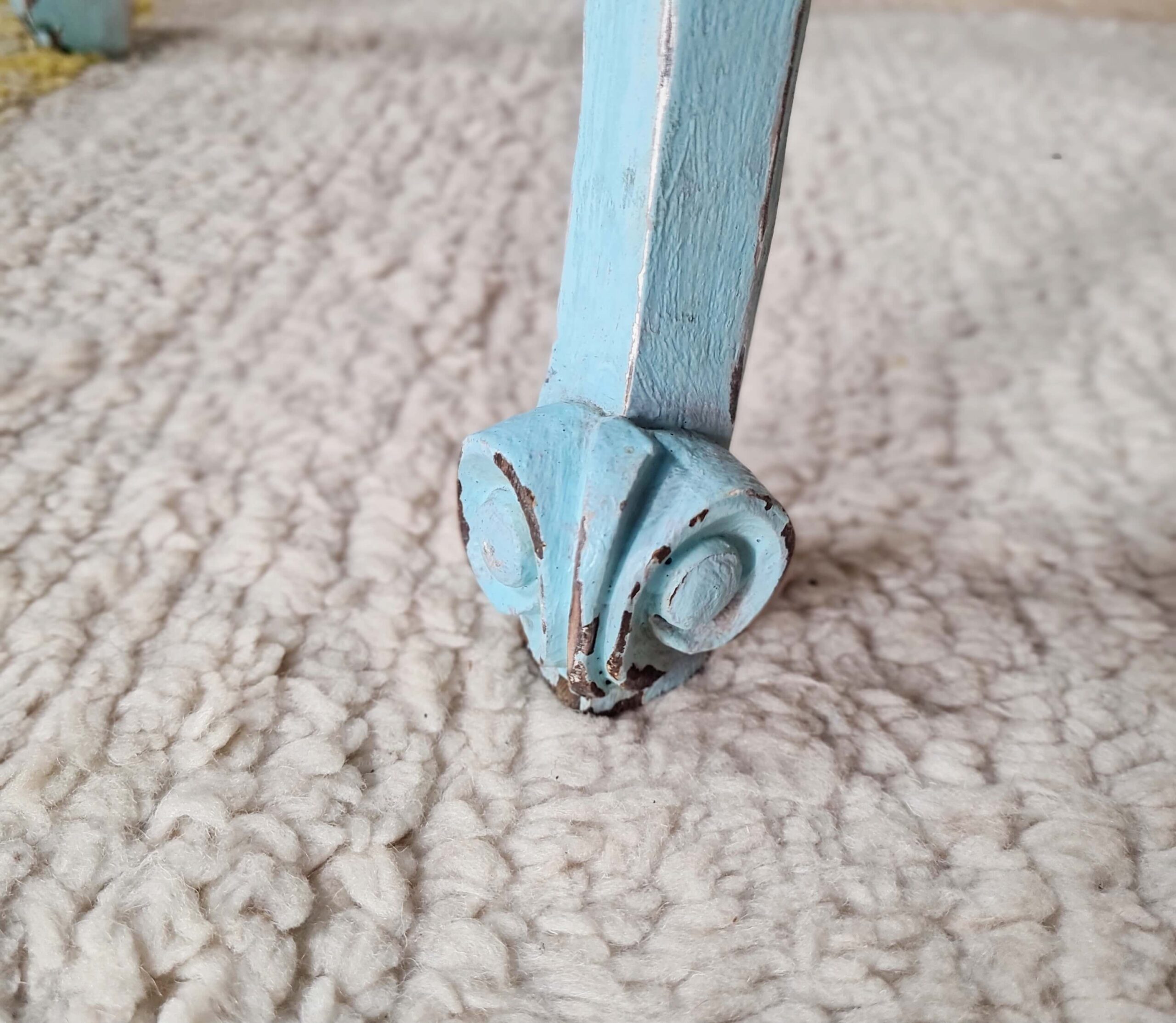Gros plan sur la volute sculptée au bas du pied d'un chevet en bois bleu turquoise