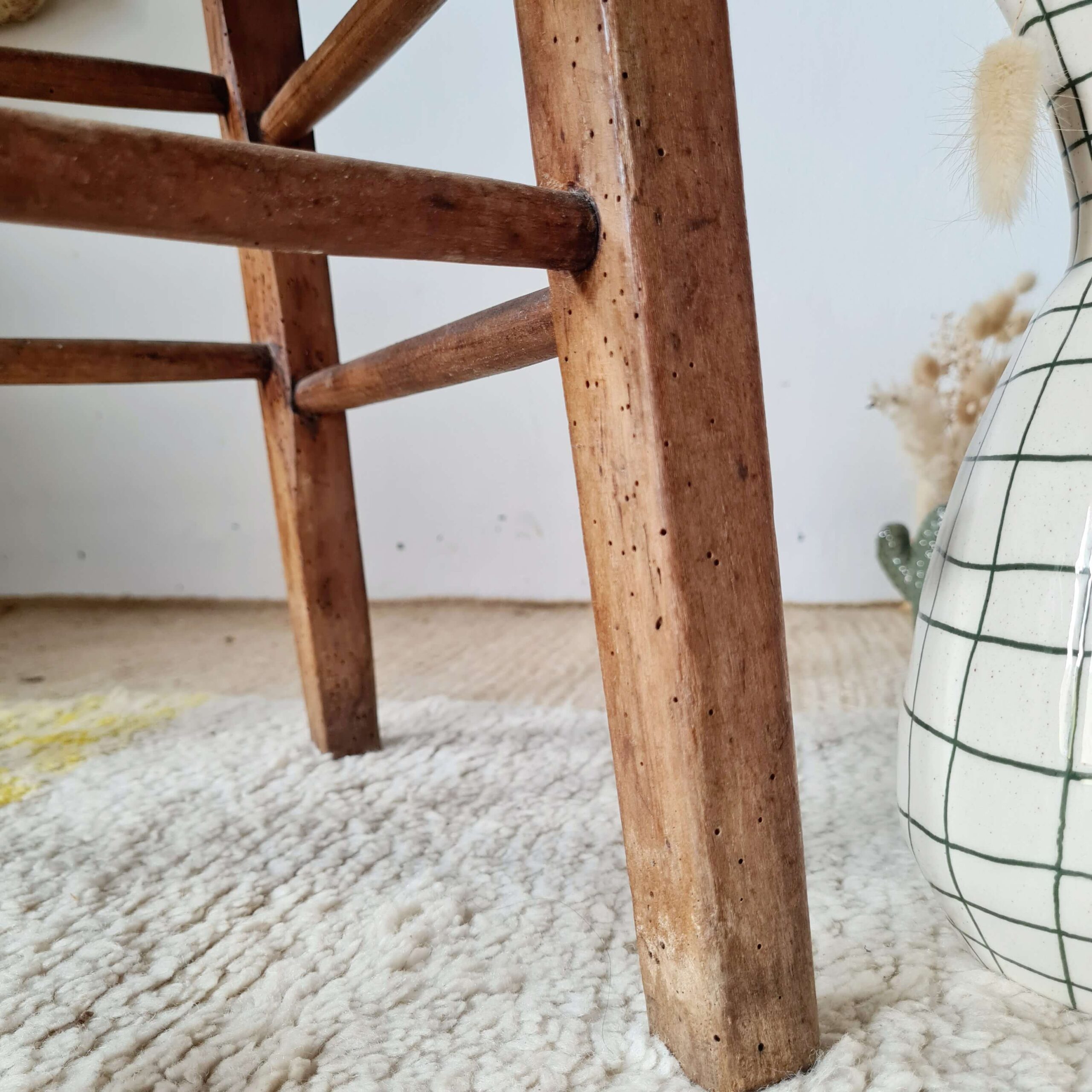 Zoom sur les pieds en bois patiné et piqués d'un tabouret rustique ancien.
