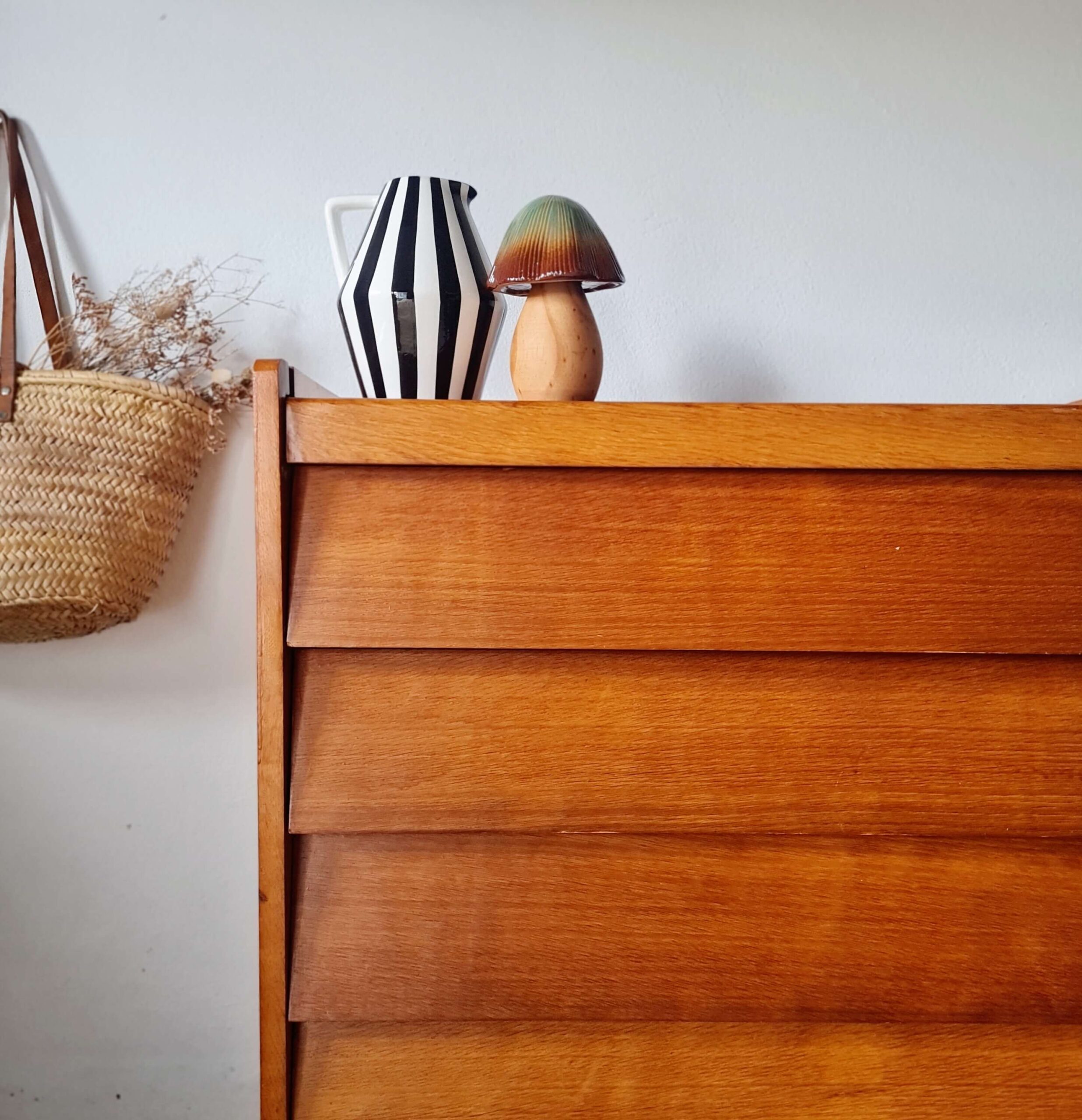 Commode vintage des années 1960 en chêne doré avec quatre tiroirs biseautés inclinés, présentée dans un décor bohème par Factory Vintage.