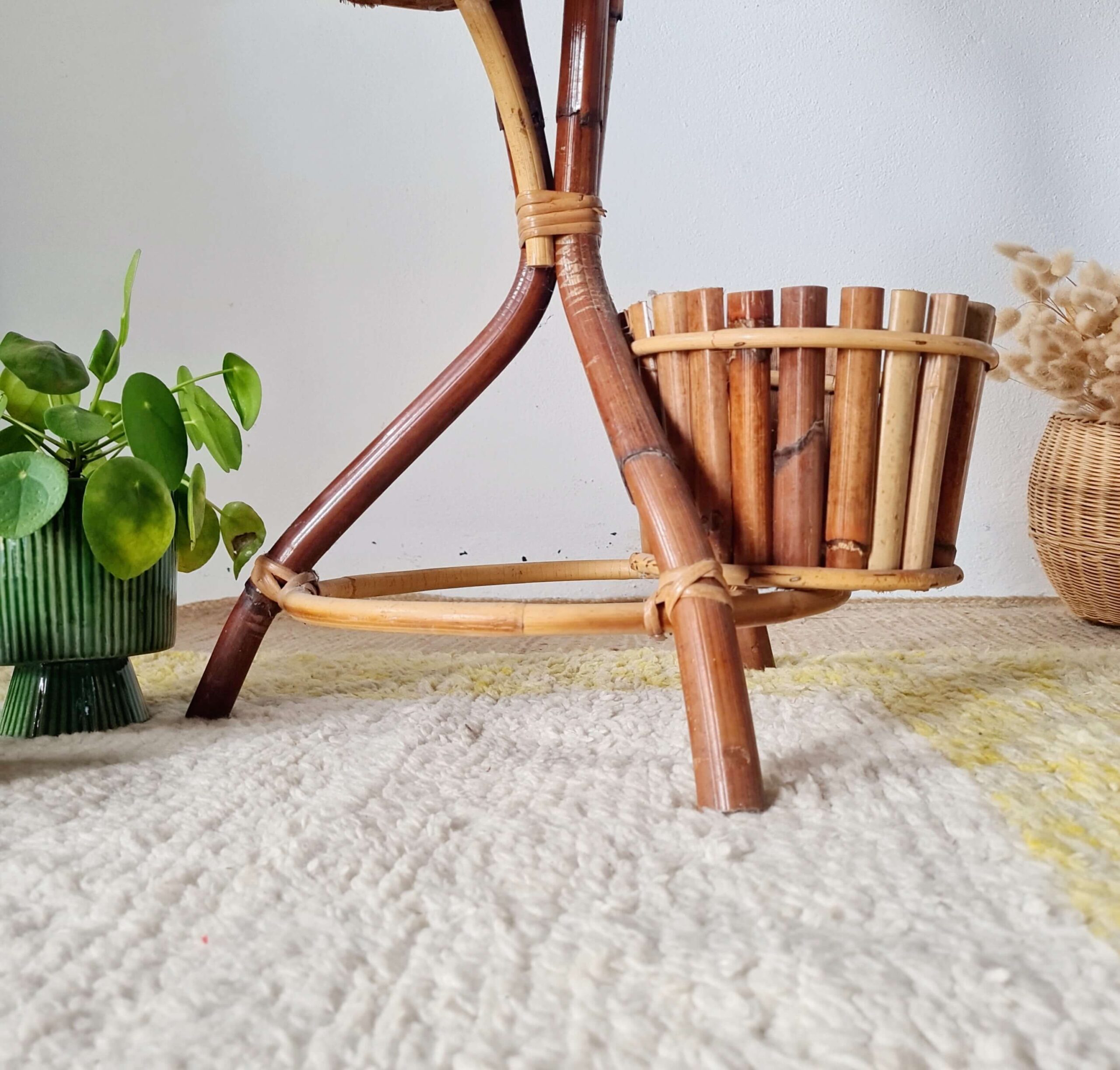 Vue de la base d'un porte-plante en bambou, avec son pot inférieur tressé en bois et un autre pot vert côtelé posé juste à côté, sur un tapis texturé.