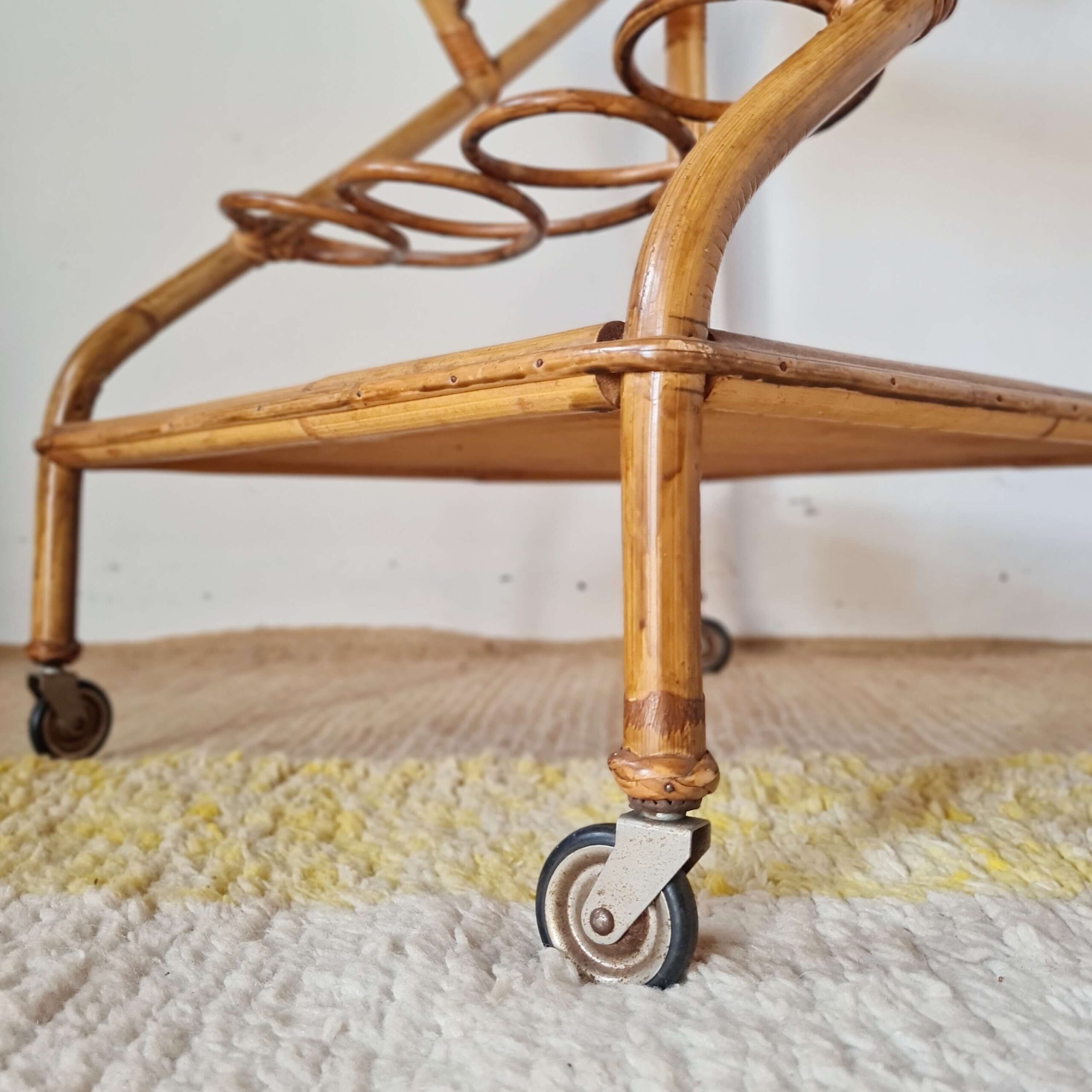 Gros plan sur une roulette en métal et le pied en rotin tressé de la desserte vintage.