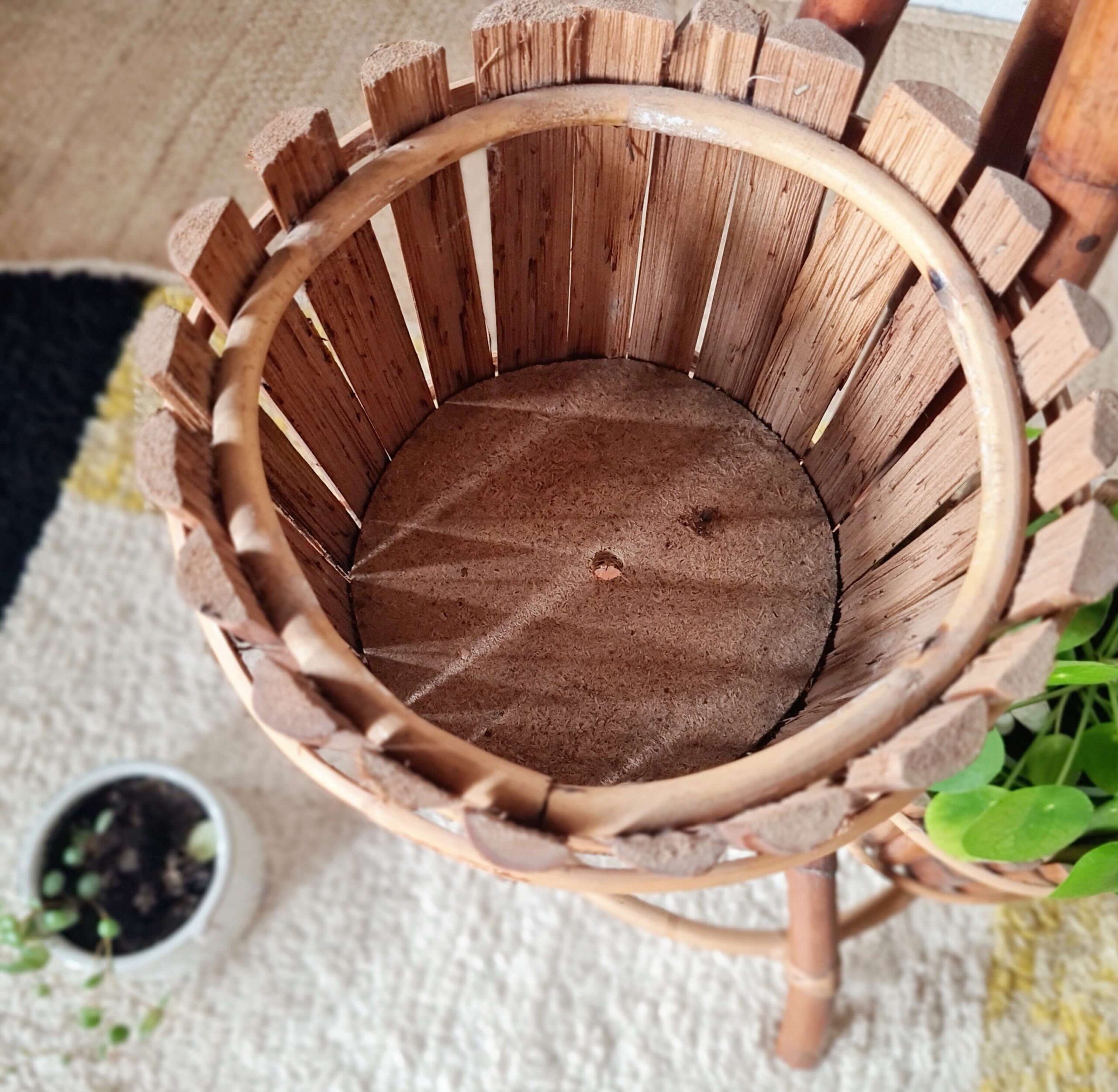 Gros plan en plongée sur l'intérieur du cache-pot supérieur vide d'un porte-plante en bambou, révélant sa structure faite de lattes de bois verticales et son fond en contreplaqué.