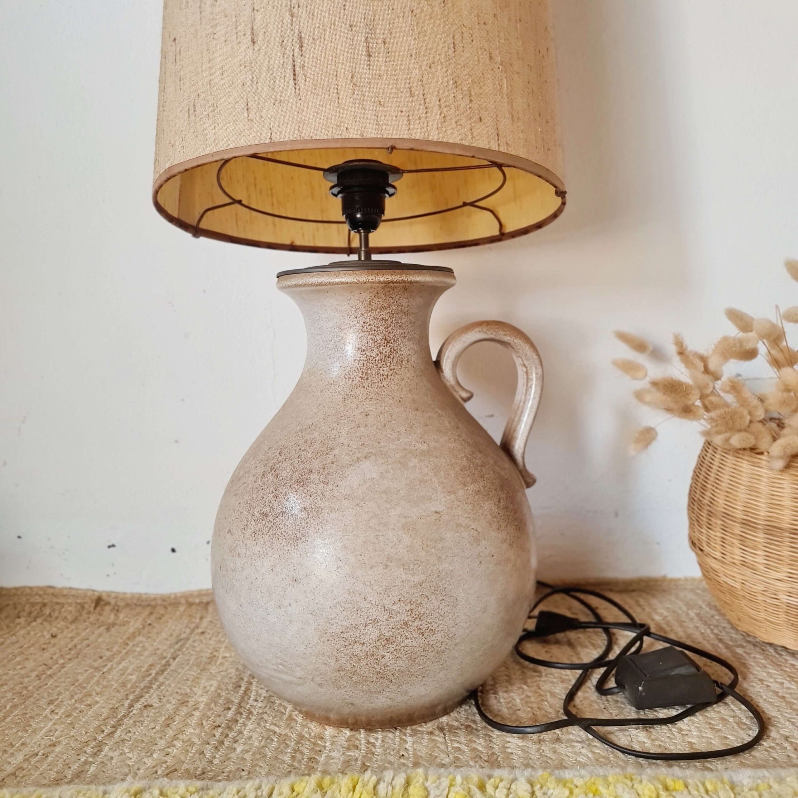 Gros plan d'une lampe en céramique artisanale avec anse et texture mouchetée.