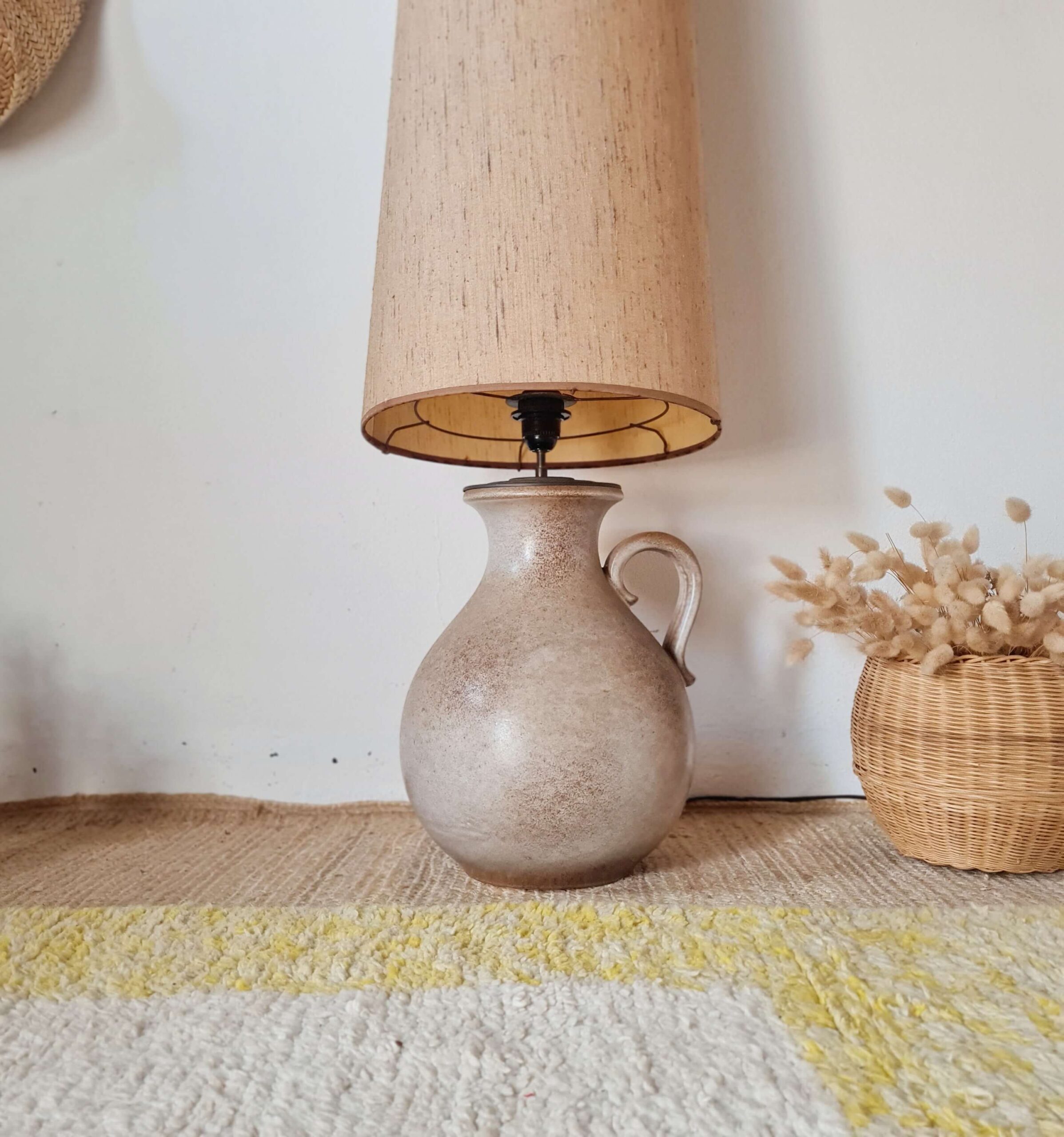 Lampe de table vintage en céramique avec anse, posée sur un tapis berbère à motifs jaunes, vue d'ensemble.