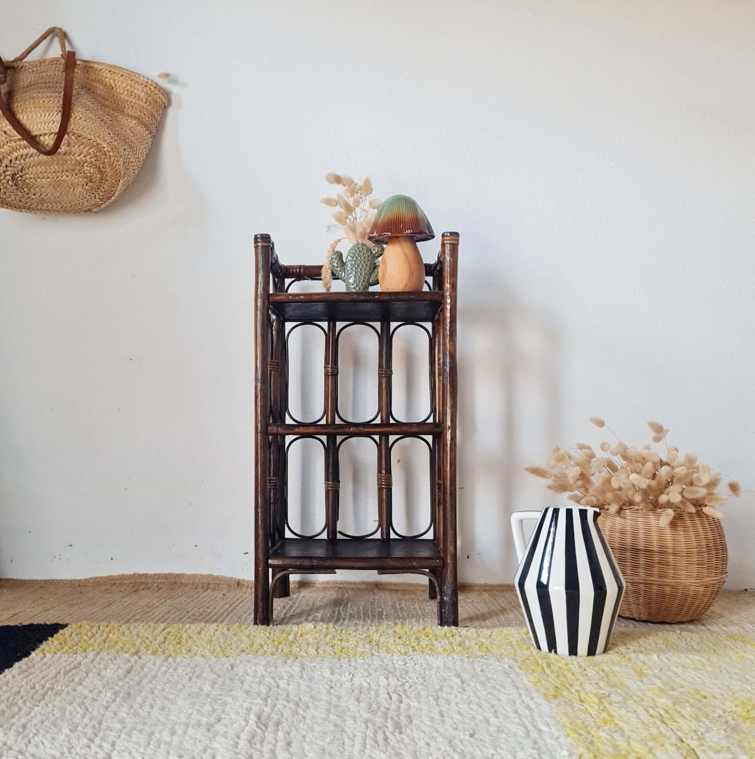 Petite bibliothèque ou étagère rétro en rotin foncé meublant un coin de pièce avec des objets de décoration.