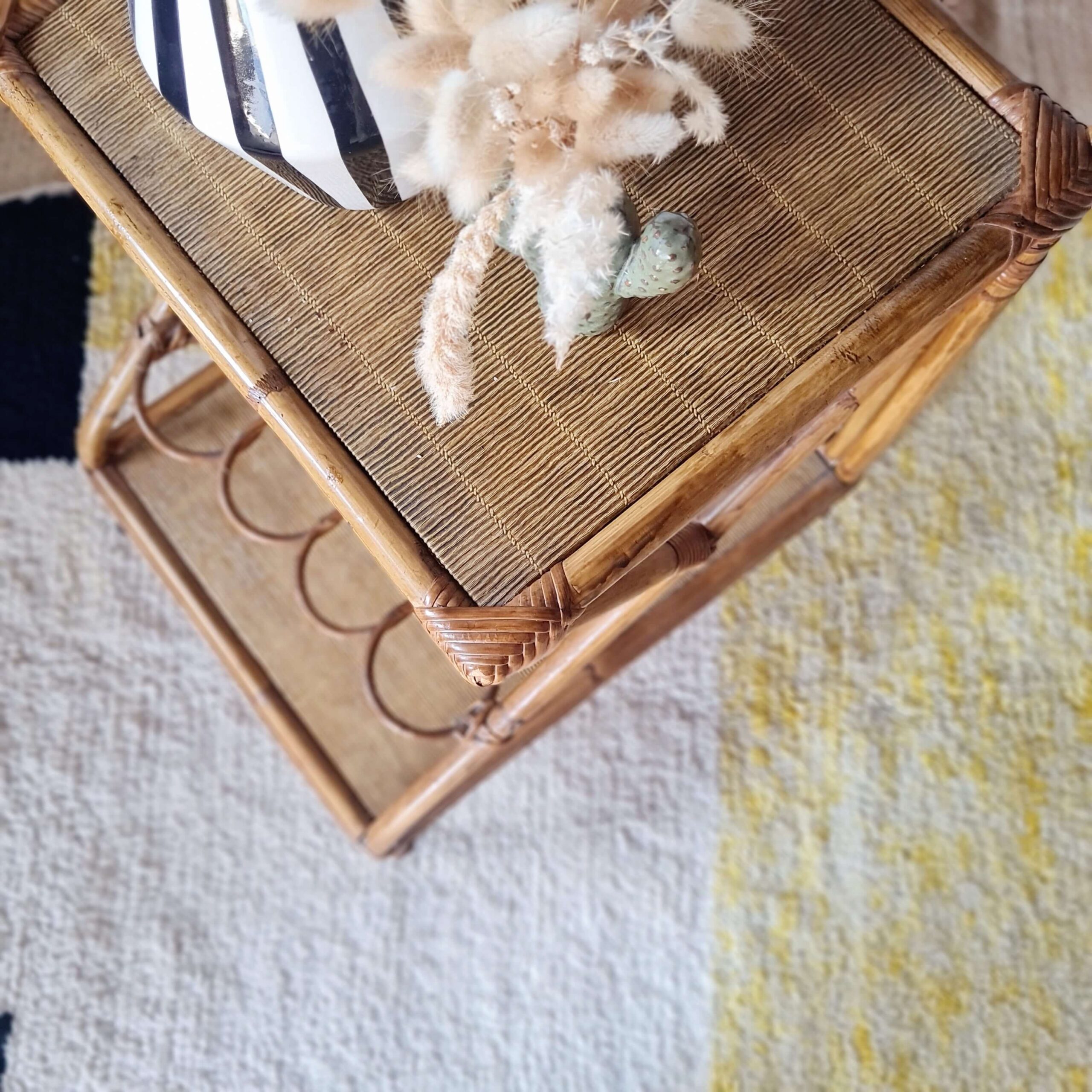 Plateau supérieur d'une desserte rétro en rotin décorée d'une cruche rayée et de fleurs séchées.