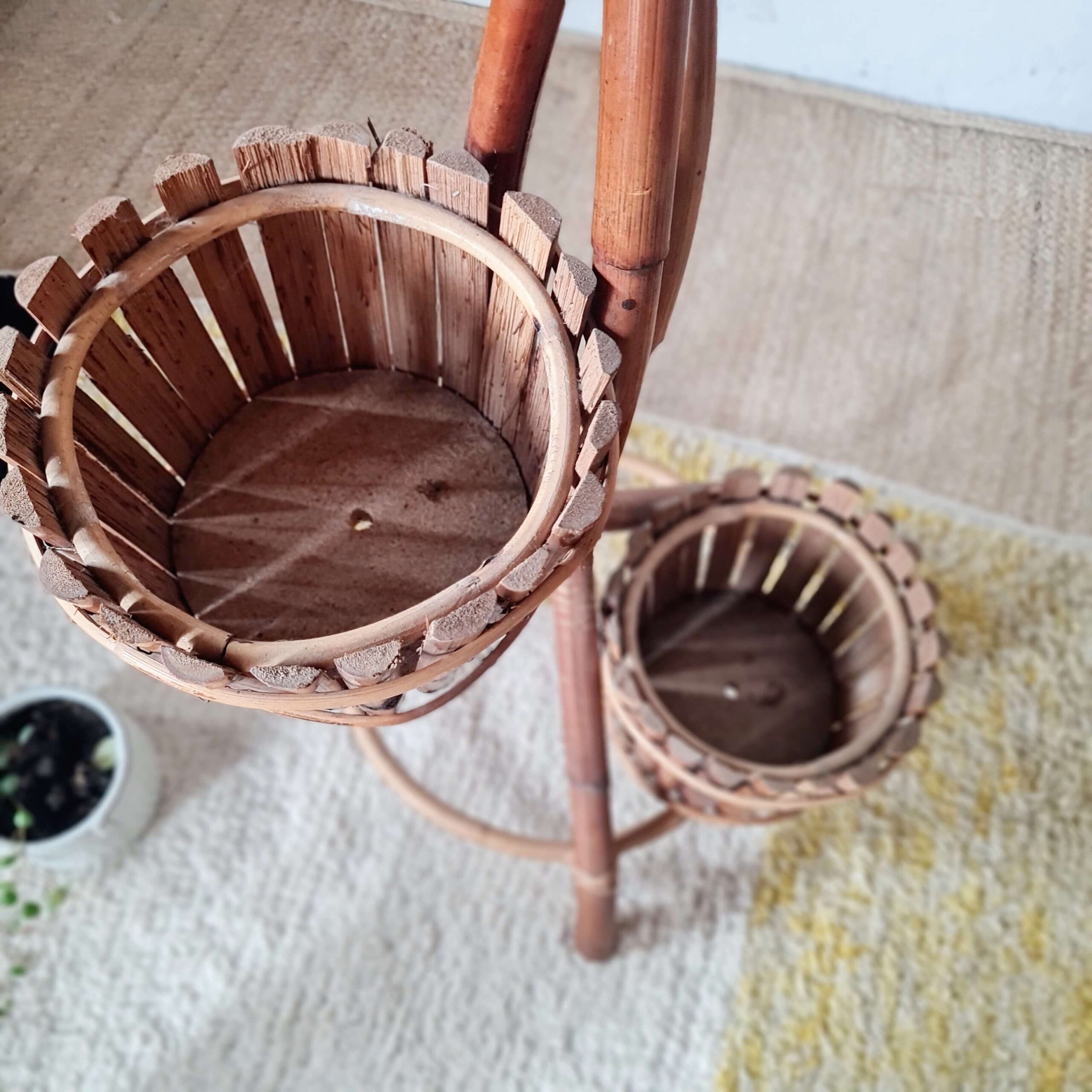 Vue en plongée du porte-plante complet en bambou et rotin, mettant en évidence la structure vide des deux cache-pots principaux et les pieds tripodes sur le tapis à motifs.