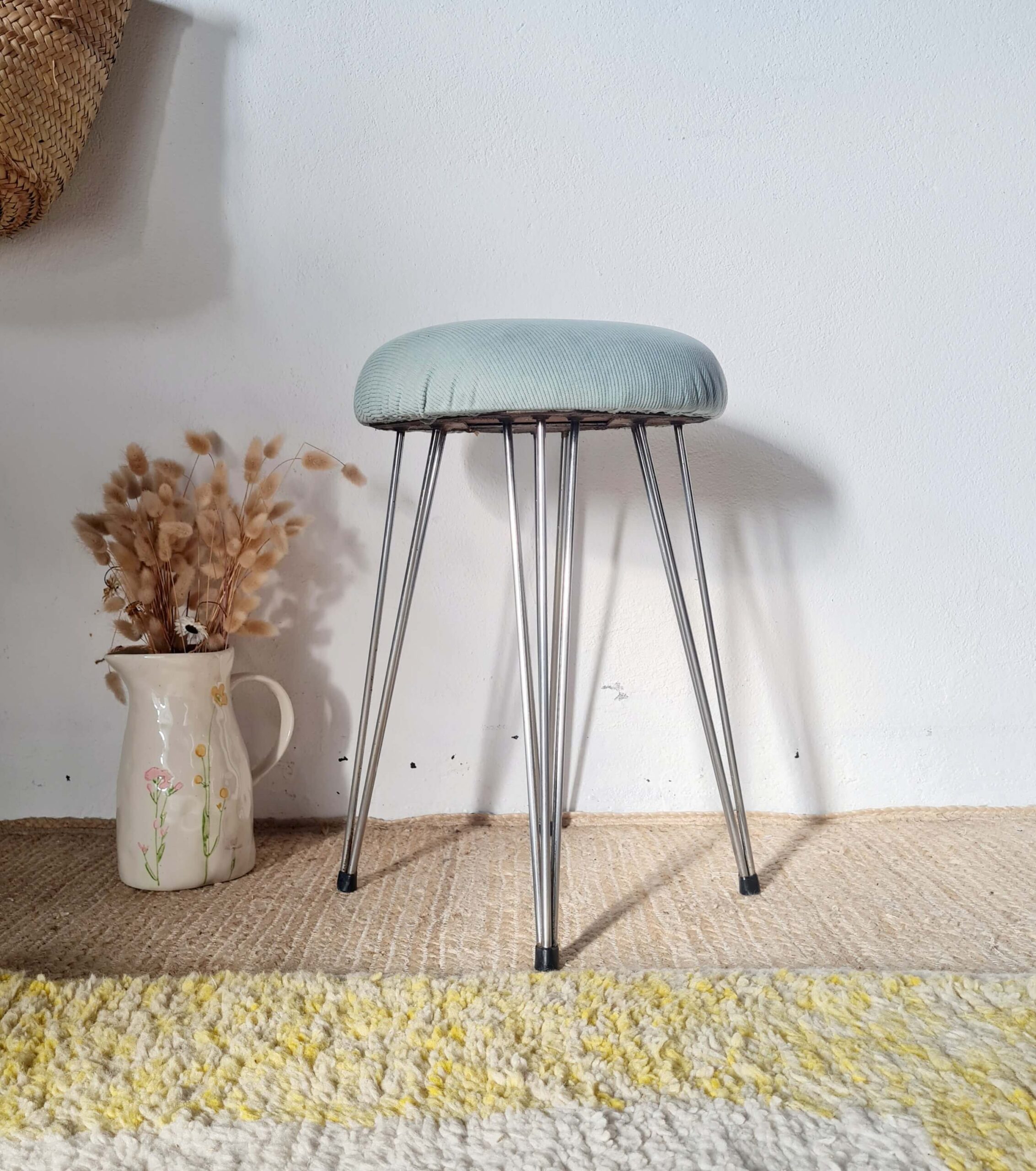 Vue de face d'un tabouret rétro avec une assise rembourrée bleue et des pieds fuselés en métal.