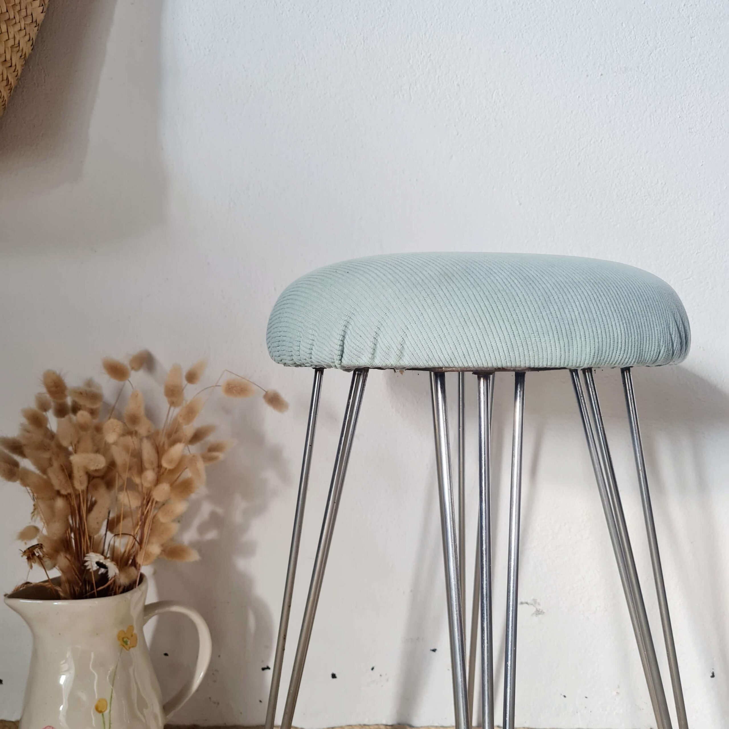 Gros plan sur l'assise en velours côtelé bleu et la structure métallique d'un tabouret vintage.
