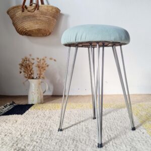 Vue d'ensemble d'un tabouret vintage avec pieds en épingle en métal et assise rembourrée bleu pastel.