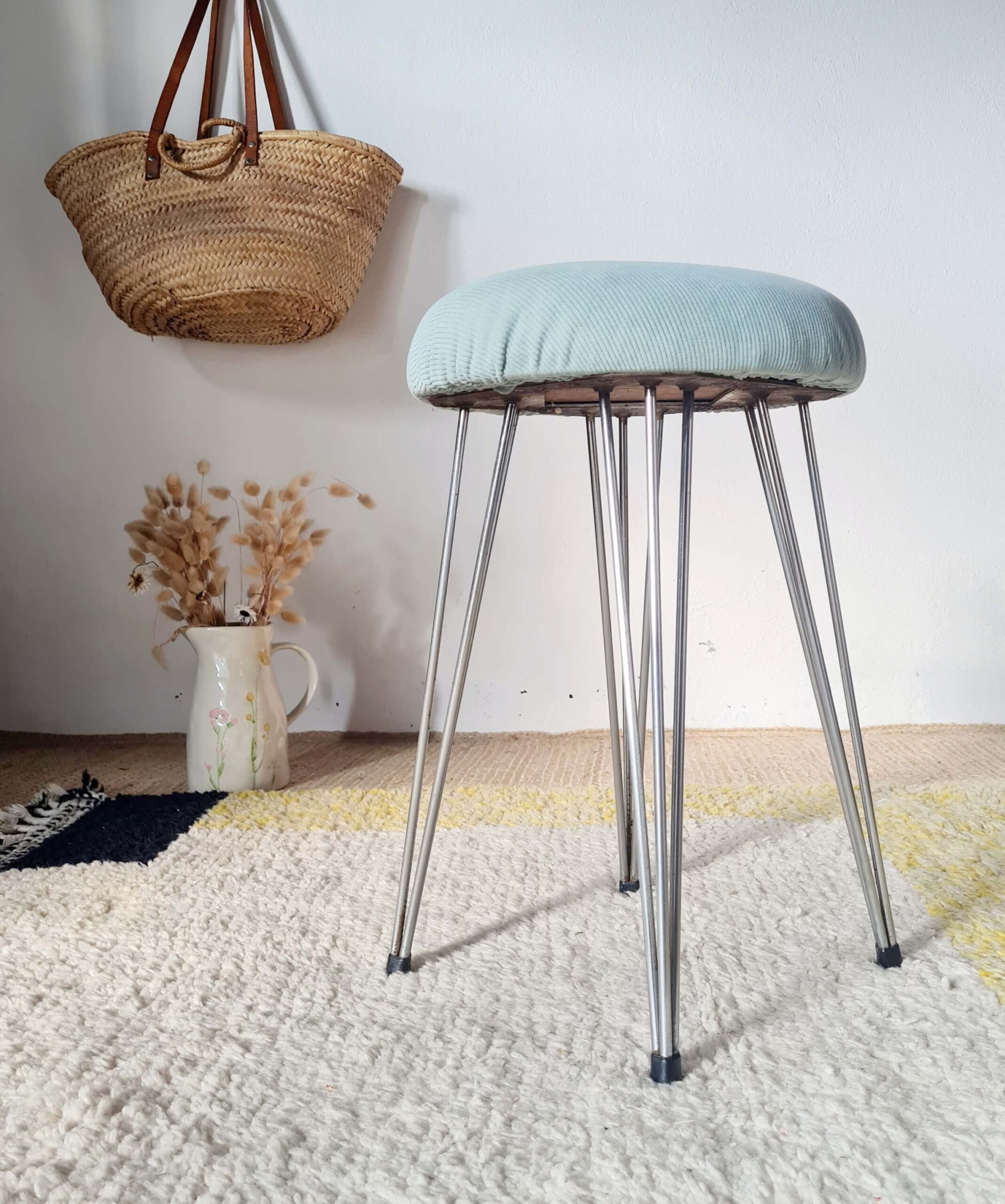 Vue d'ensemble d'un tabouret vintage avec pieds en épingle en métal et assise rembourrée bleu pastel.