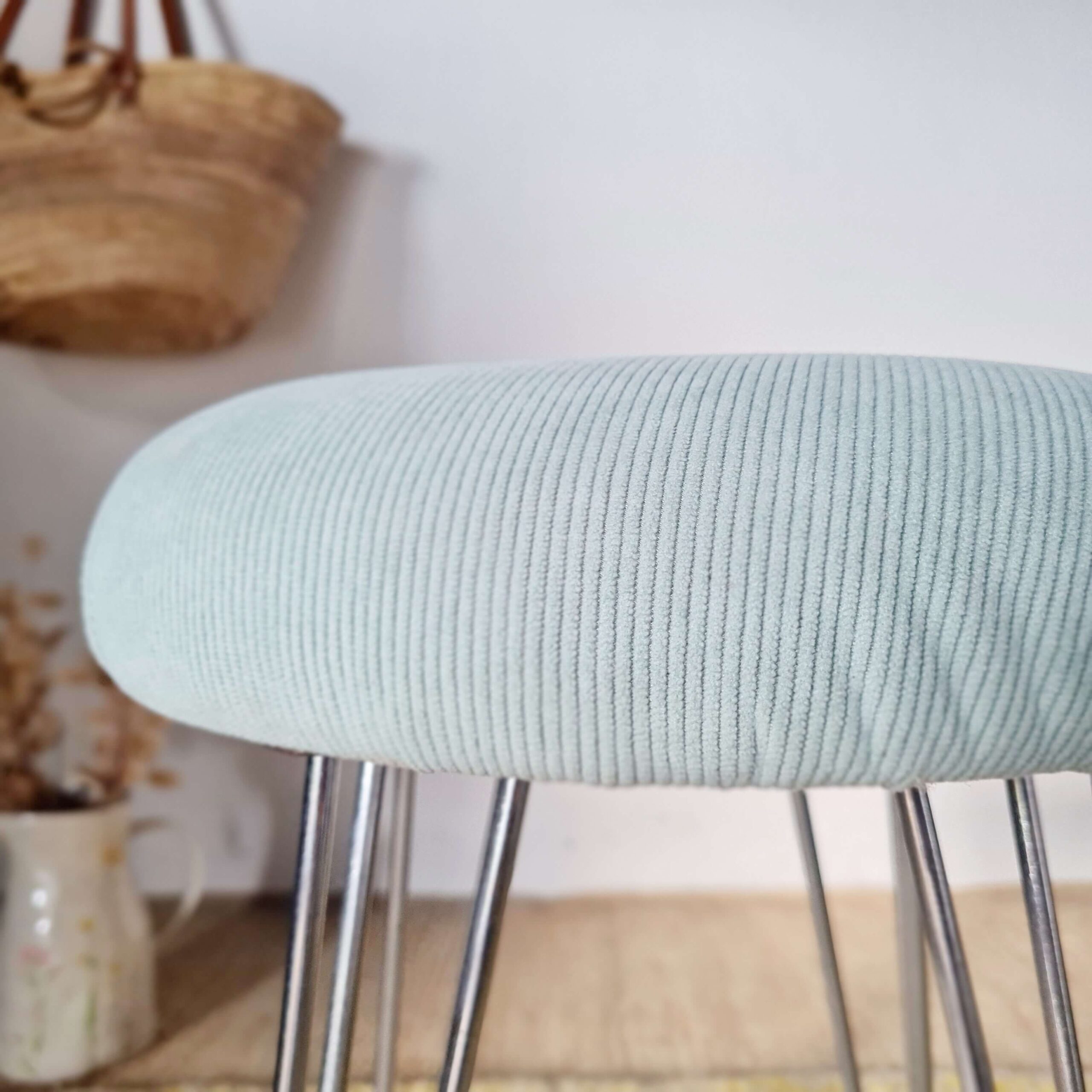 Vue de trois quarts d'un tabouret vintage au piètement fuselé en métal et assise en velours côtelé bleu.