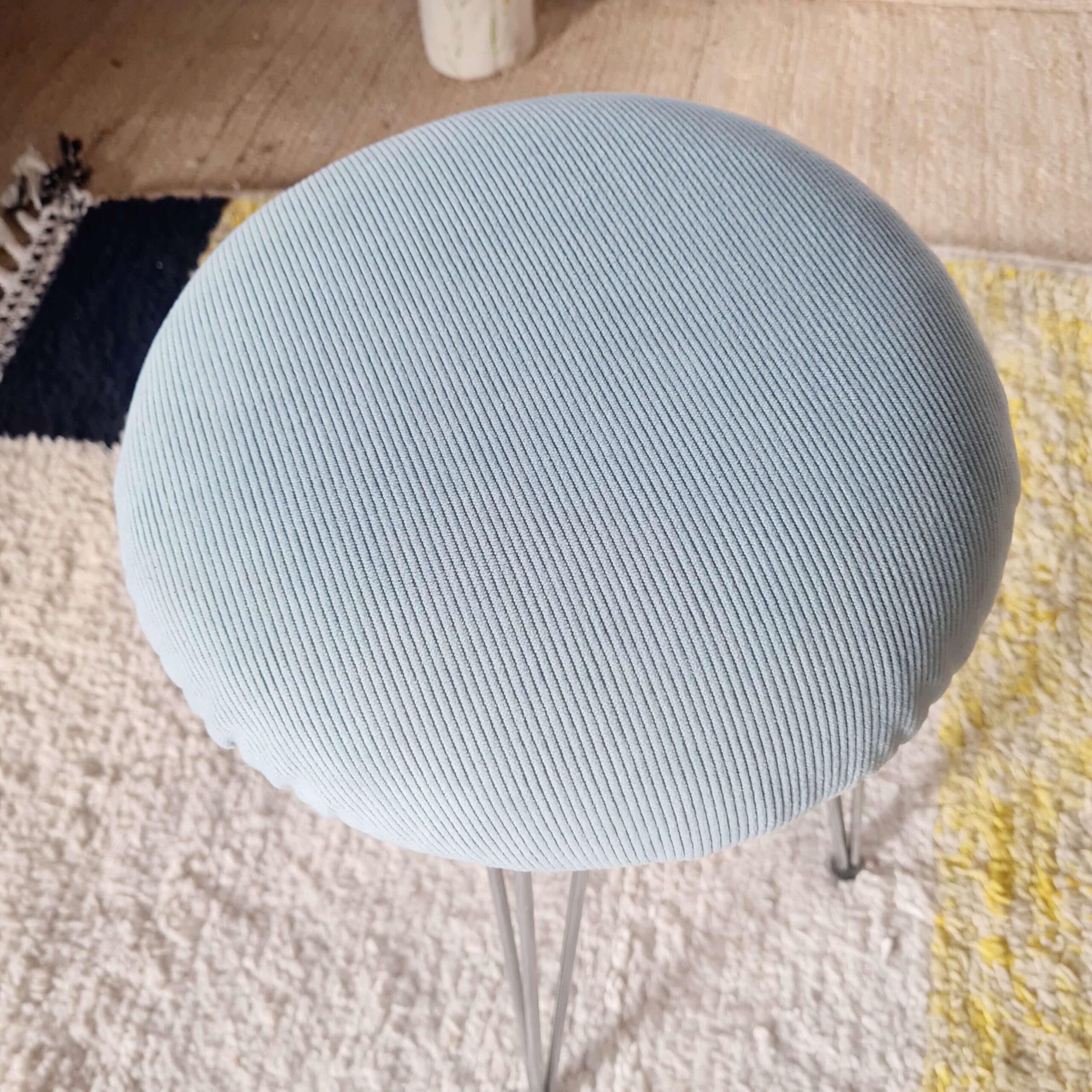 Vue en plongée centrée sur l'assise ronde en velours côtelé bleu clair du tabouret vintage.