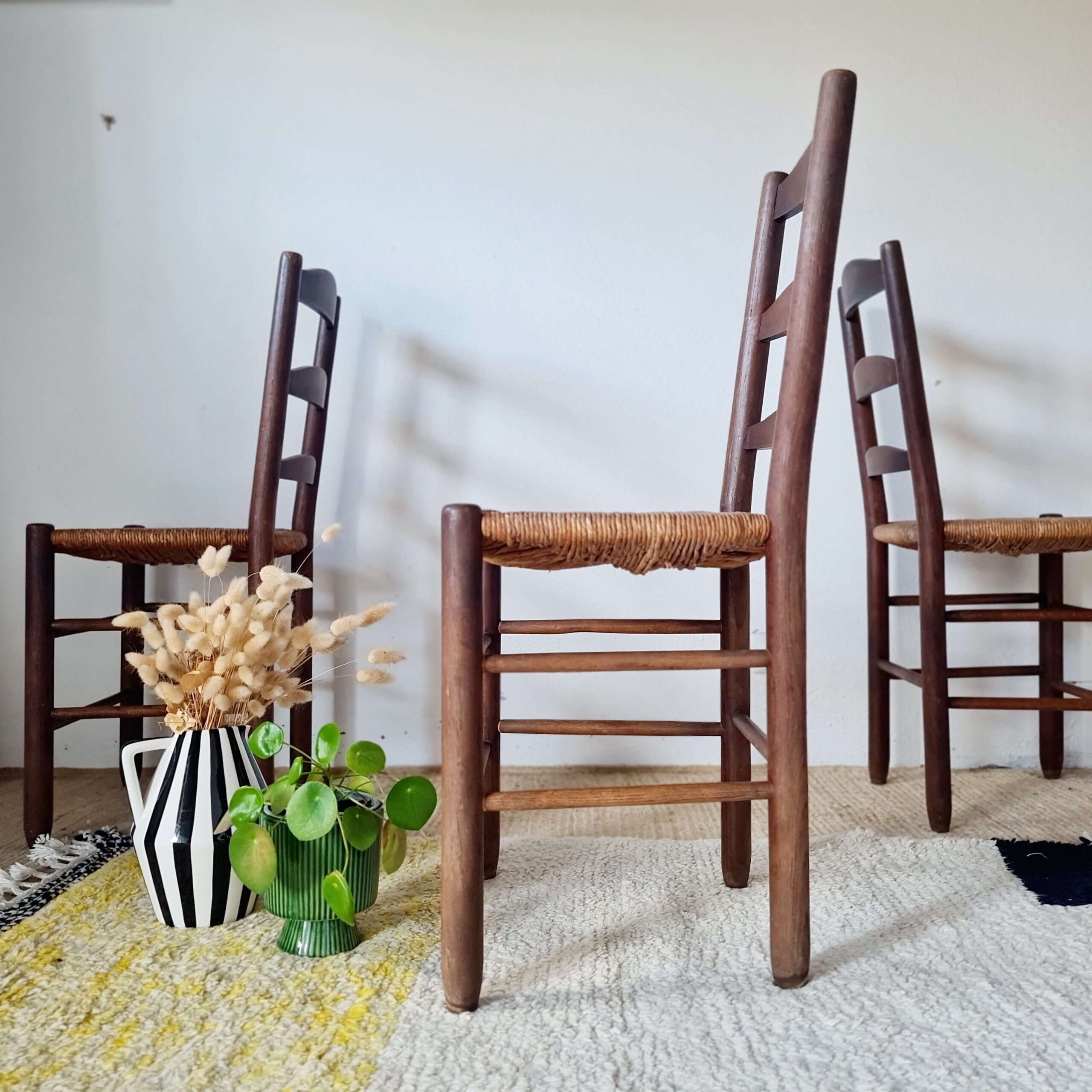 Ensemble de trois chaises anciennes en châtaignier et paille tressée, alignées de face sur un tapis berbère à motifs géométriques jaunes et noirs.