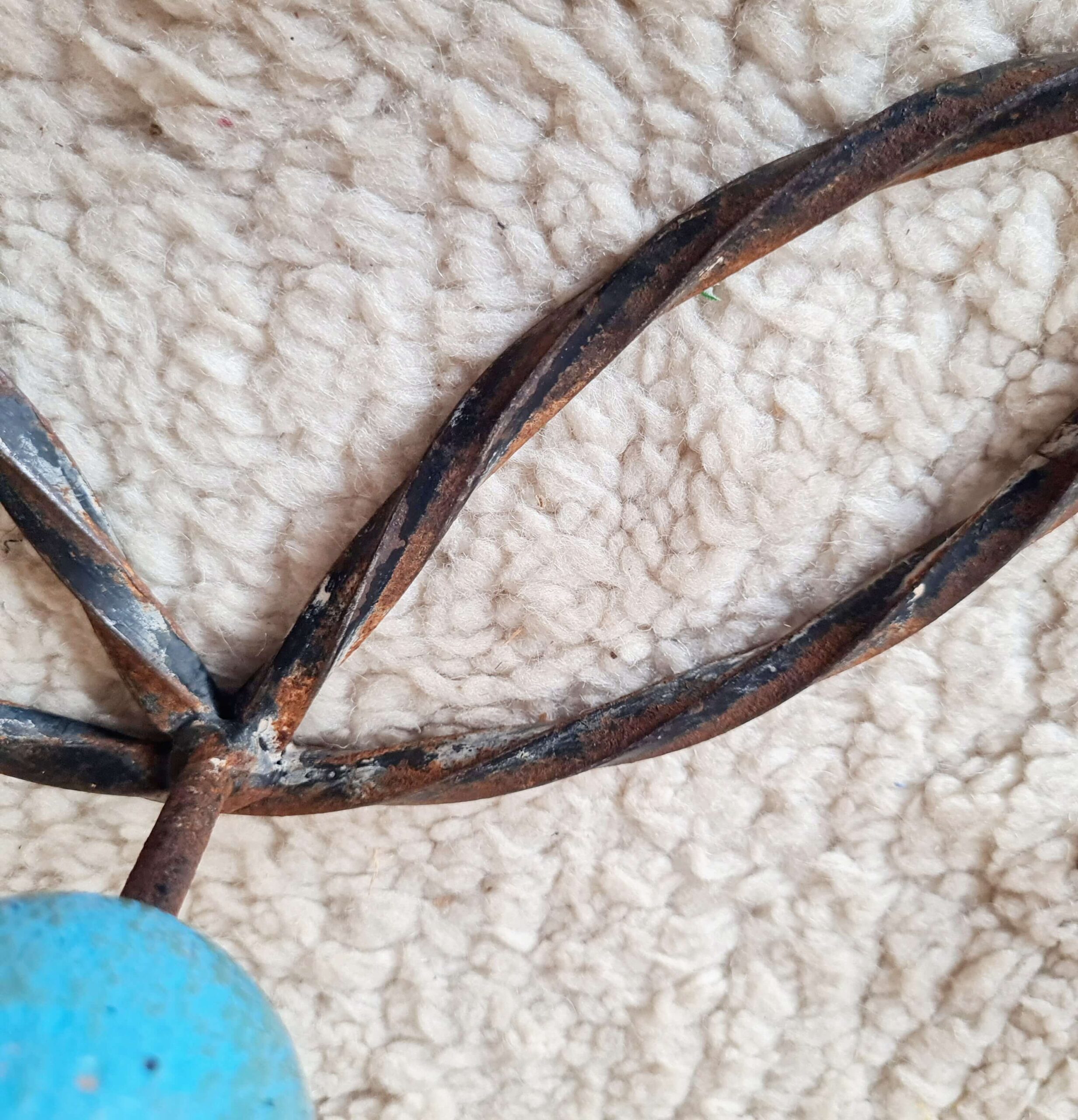 Gros plan macro sur la patine rouillée et la torsion artisanale du métal foncé d'un porte-manteau mural ancien.