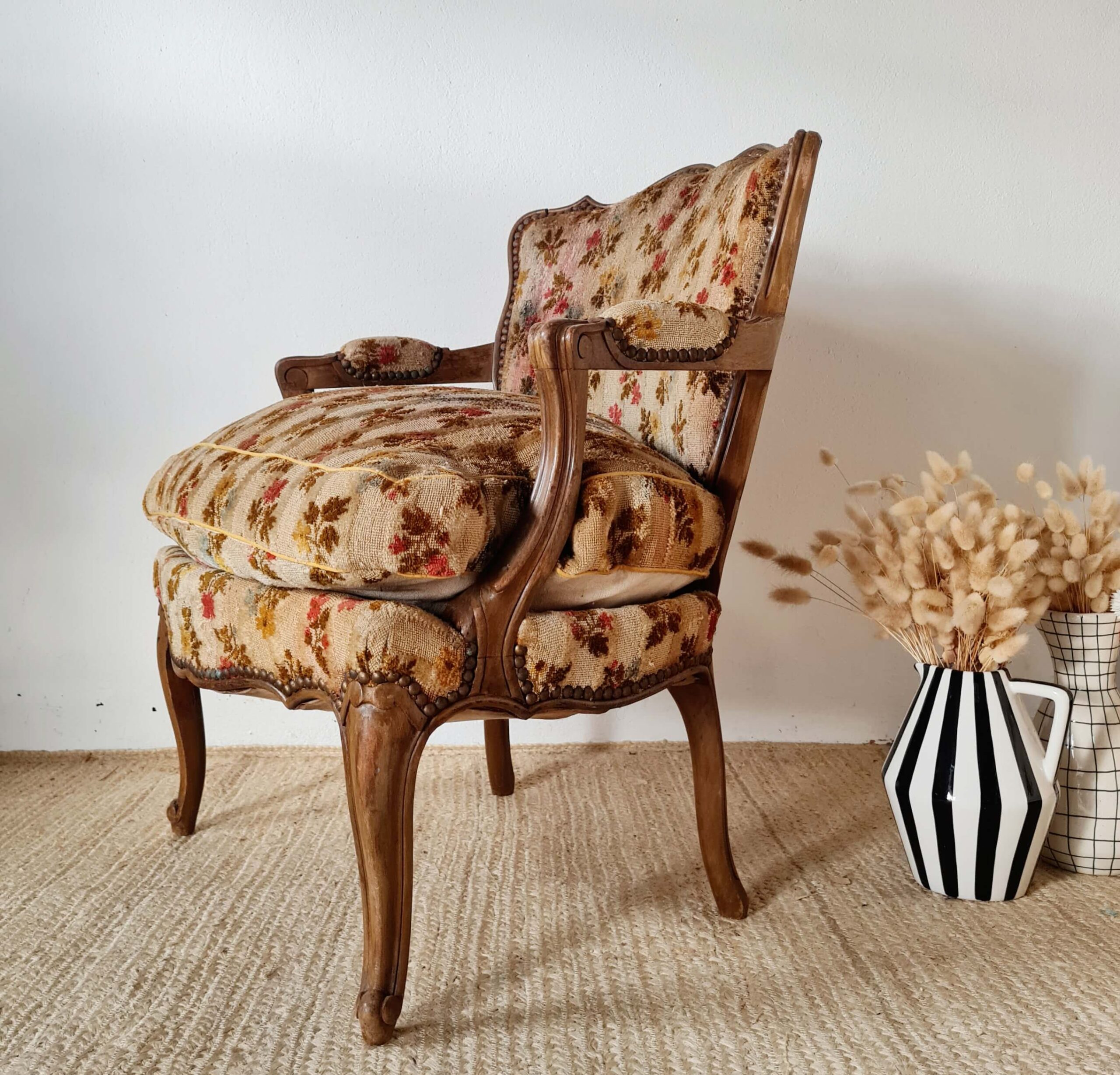 Vue de trois quarts en plongée sur le côté droit du fauteuil, soulignant la richesse du tissu tapissier aux motifs floraux variés (rouge, jaune) et la patine du bois clair de la structure apparente.