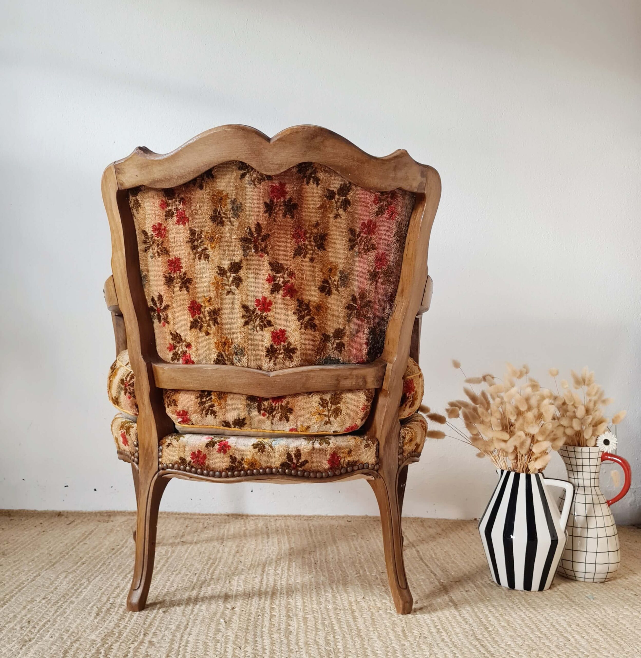Vue arrière du fauteuil crapaud. Le dossier présente une forme chantournée en bois sculpté qui encadre le tissu tapissier. La structure en bois est visible sur toute la hauteur du dossier et les quatre pieds.