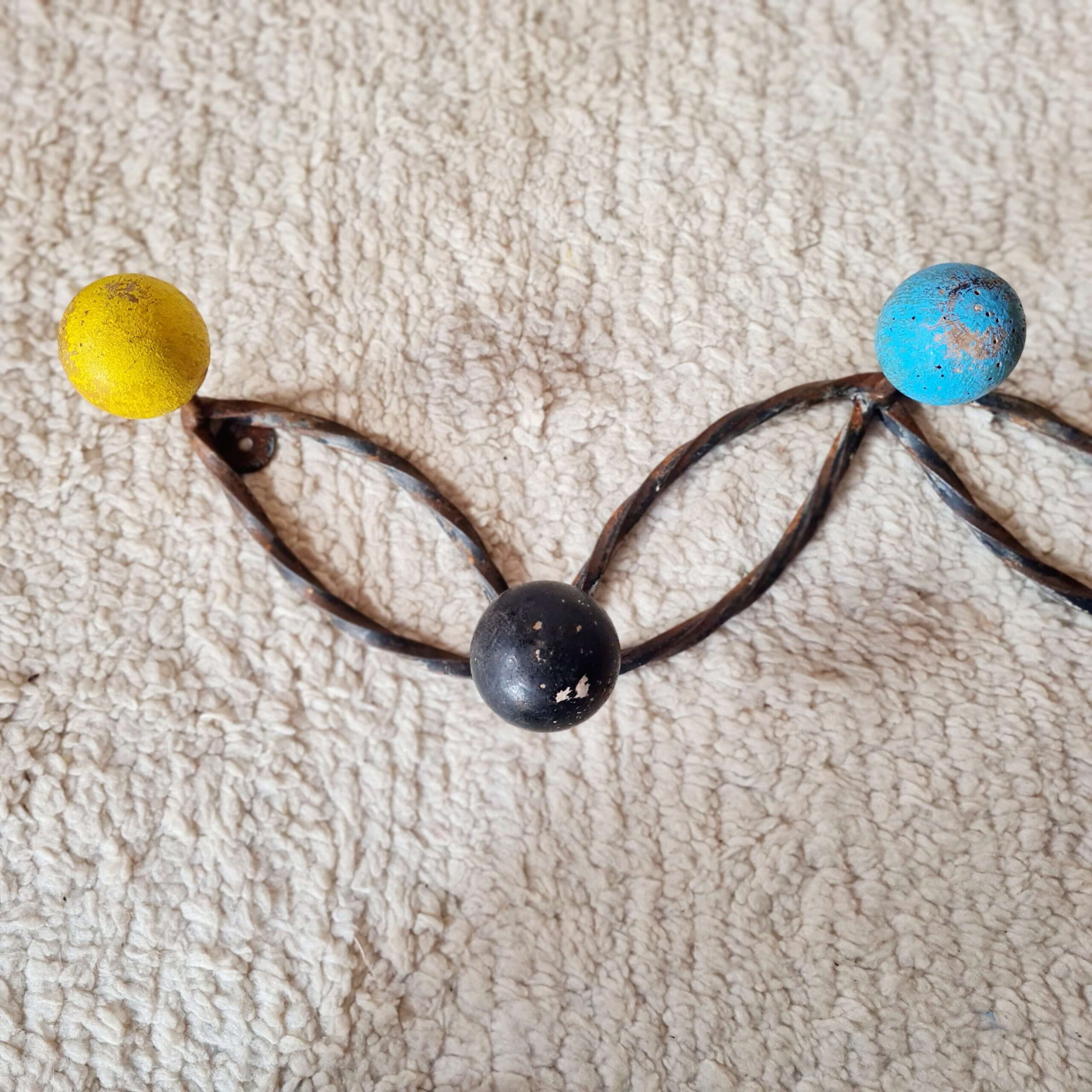Vue rapprochée sur une section d'une patère murale vintage montrant une boule jaune, une noire et une bleue sur fond de tapis écru texturé.