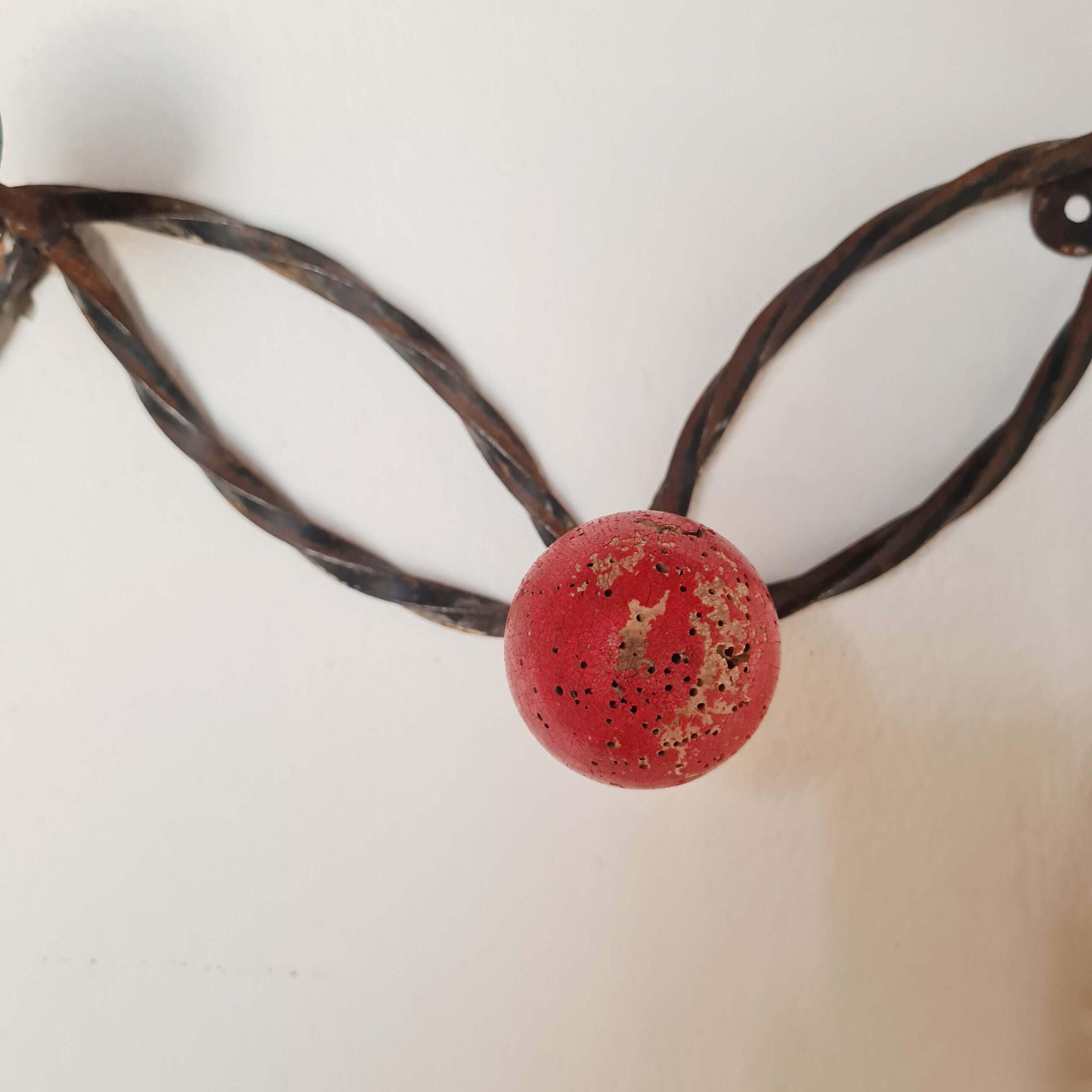 Gros plan sur une boule en bois rouge patinée par le temps fixée sur la structure en métal torsadé d'une patère vintage.
