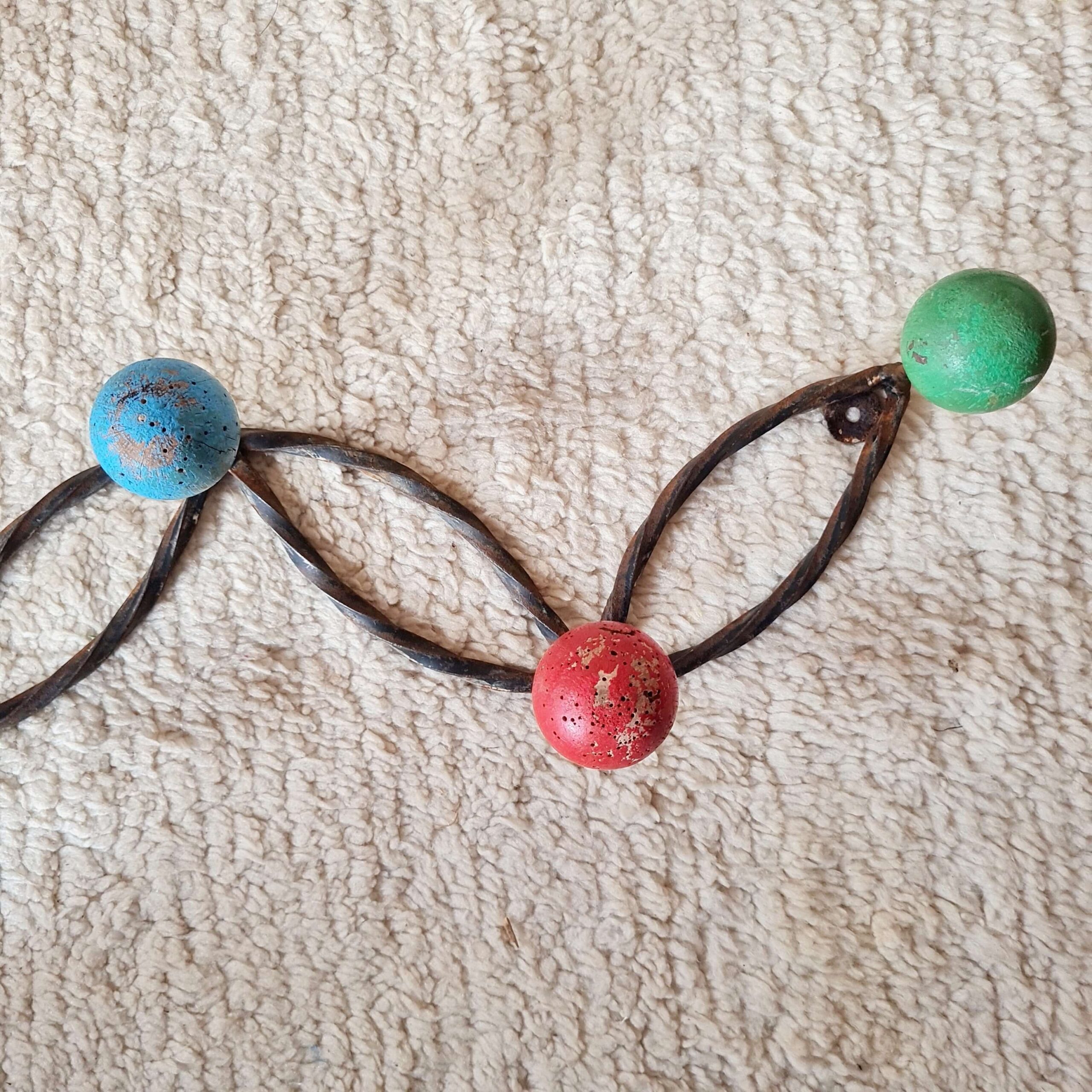 Vue de trois quarts d'un porte-manteau mural style fifties aux boules colorées et attaches métalliques murales apparentes.