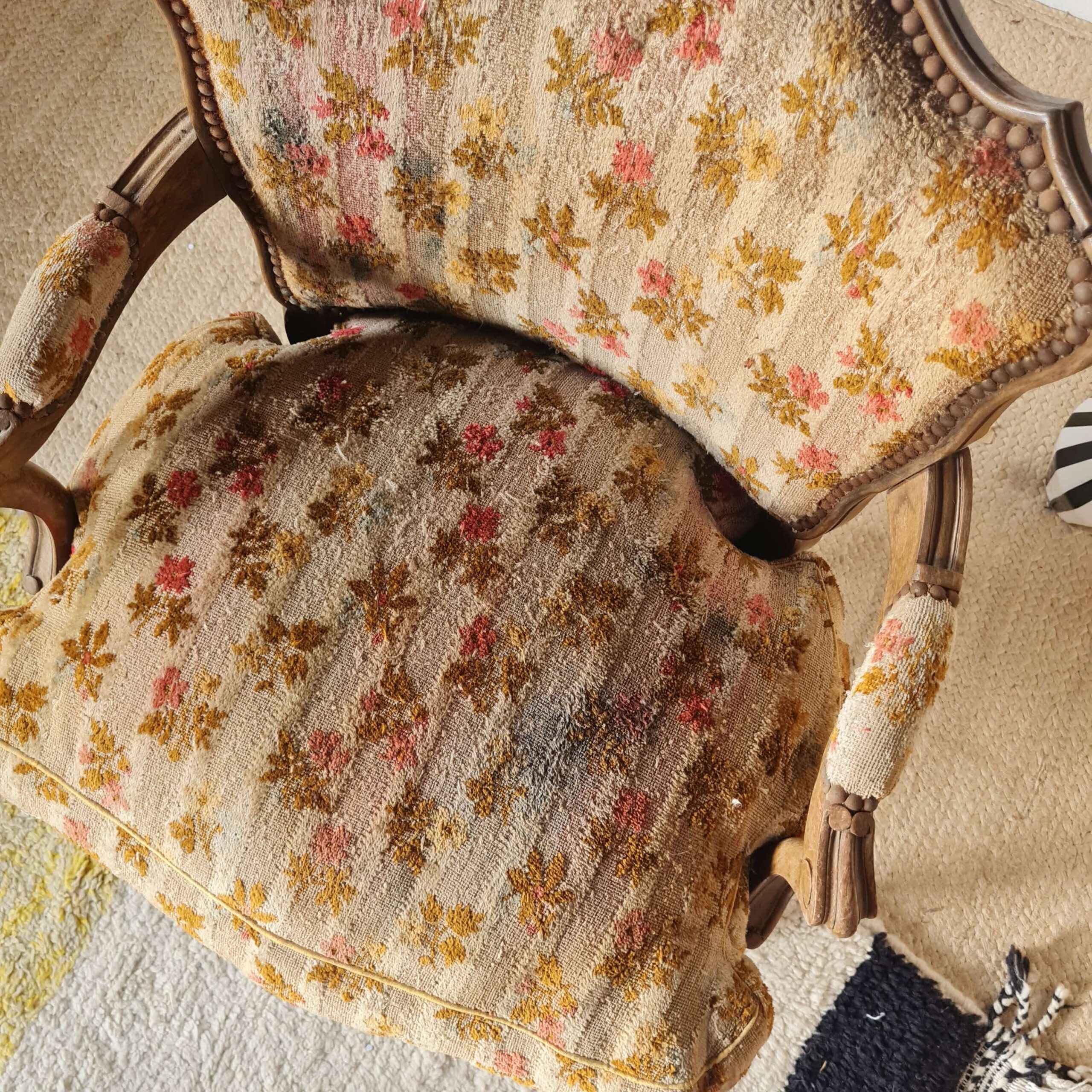 Vue en plongée et de profil gauche du fauteuil crapaud, montrant la continuité du tissu fleuri sur l'accoudoir et le dossier, ainsi que la forme élégante des pieds arrière et de la traverse en bois sculpté.