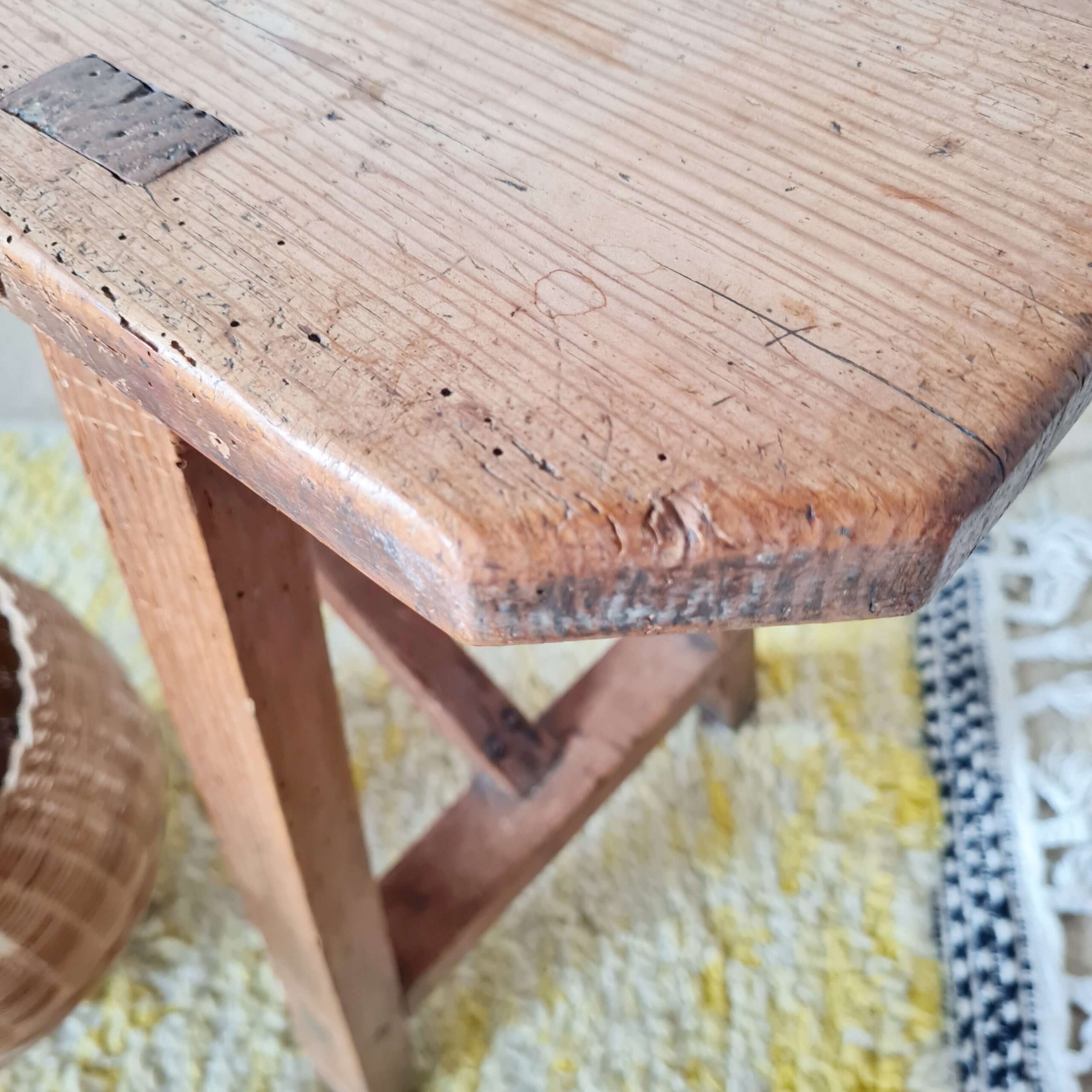 Gros plan sur l'angle d'une assise de banc ancien en bois massif, révélant la technique d'assemblage en tenon-mortaise et une patine ancienne.