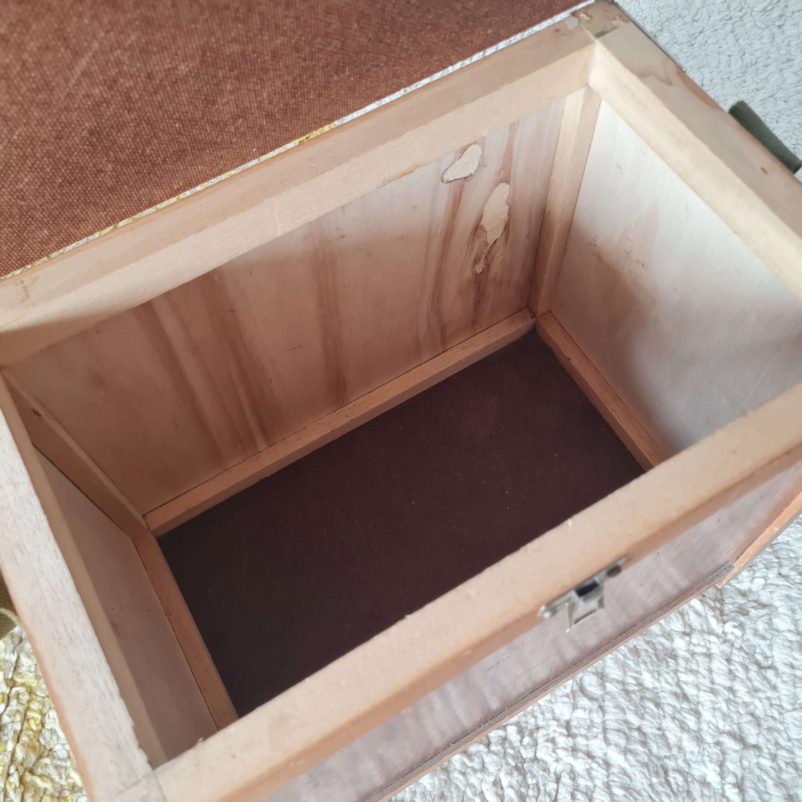 Gros plan sur le fond et les parois en bois brut du compartiment de rangement de l'ancien tabouret de pêcheur.