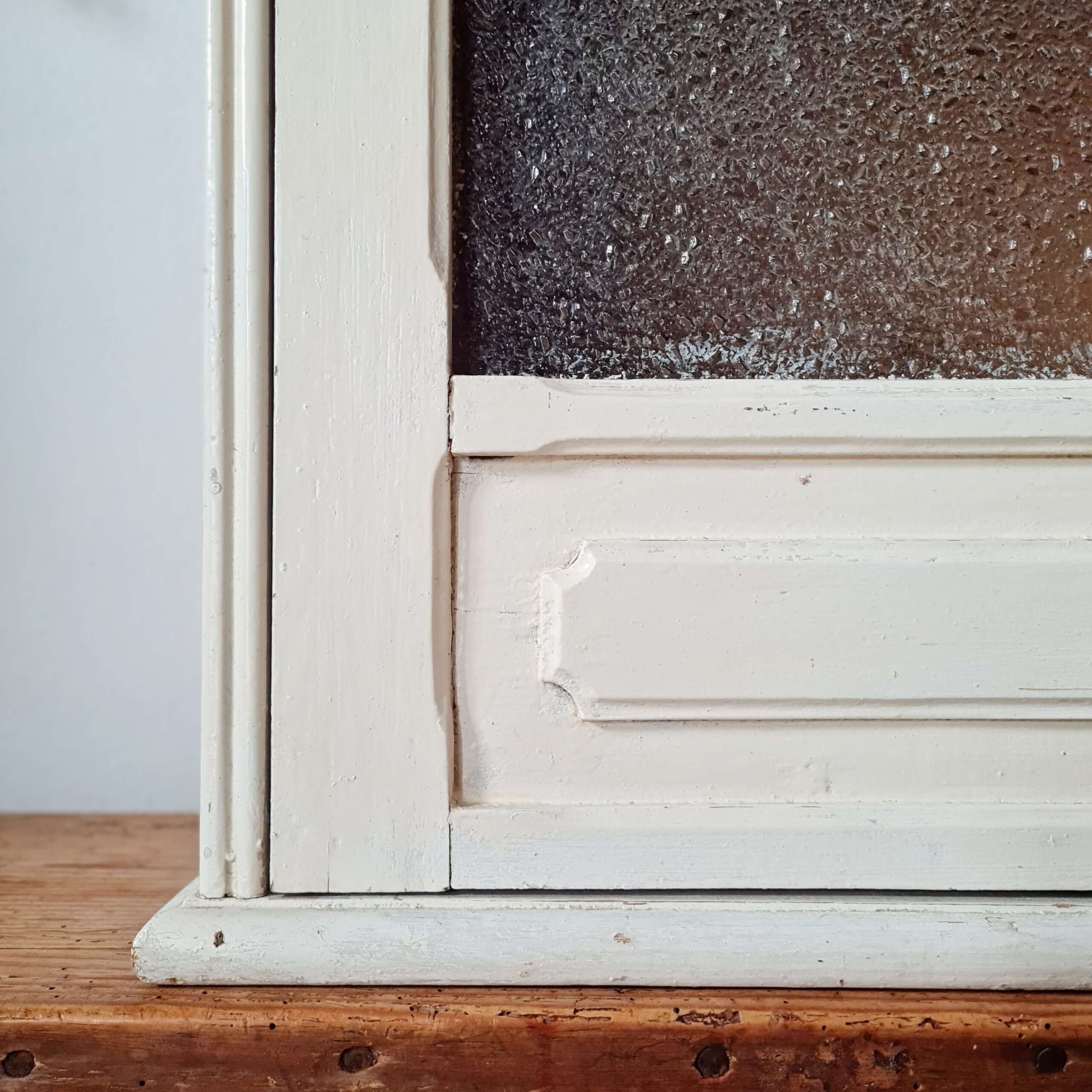Gros plan sur le coin inférieur gauche de la petite vitrine murale, montrant les détails des moulures du panneau bas et la peinture blanche patinée.