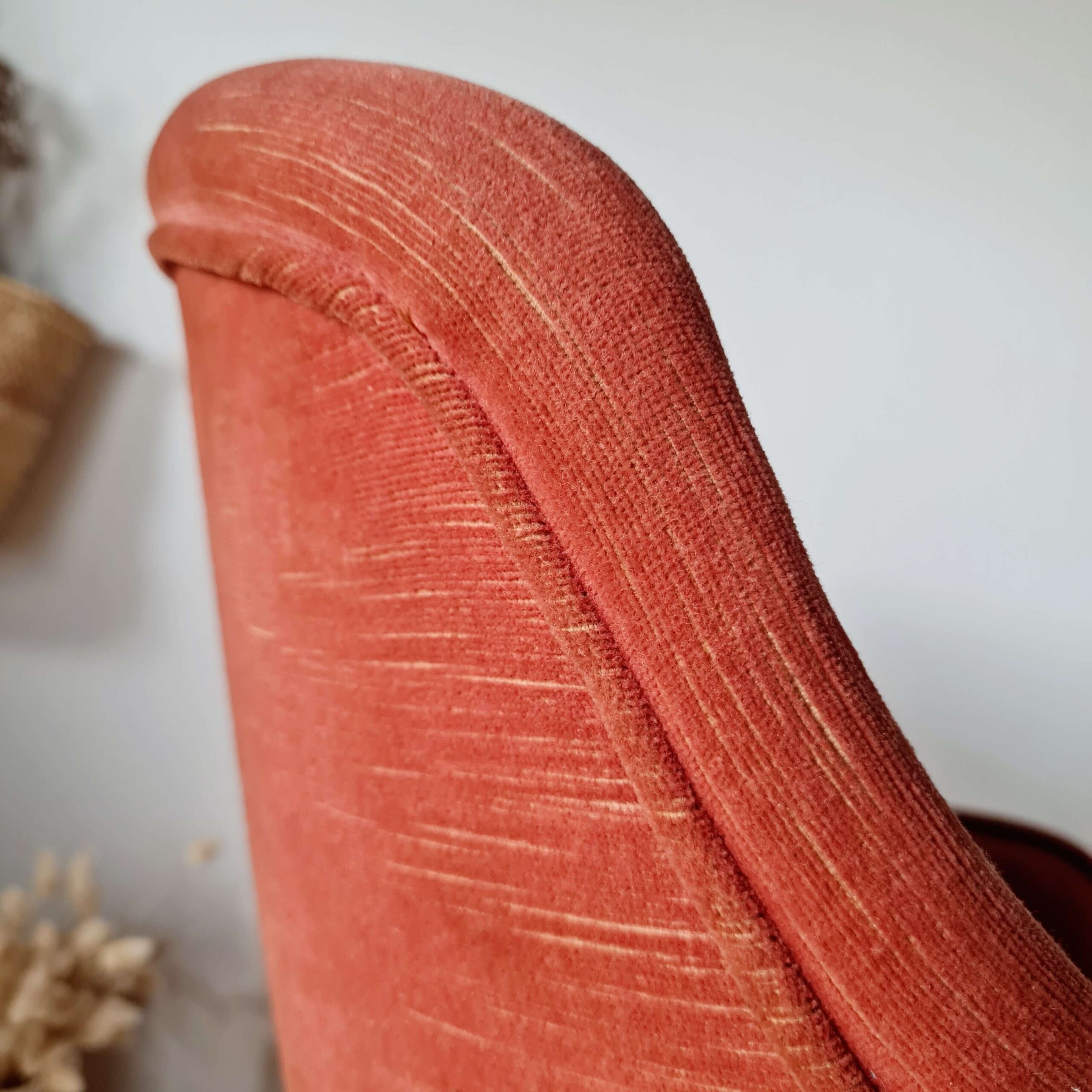 Gros plan sur le passepoil et les coutures du dossier d'un fauteuil crapaud ancien en tissu texturé.