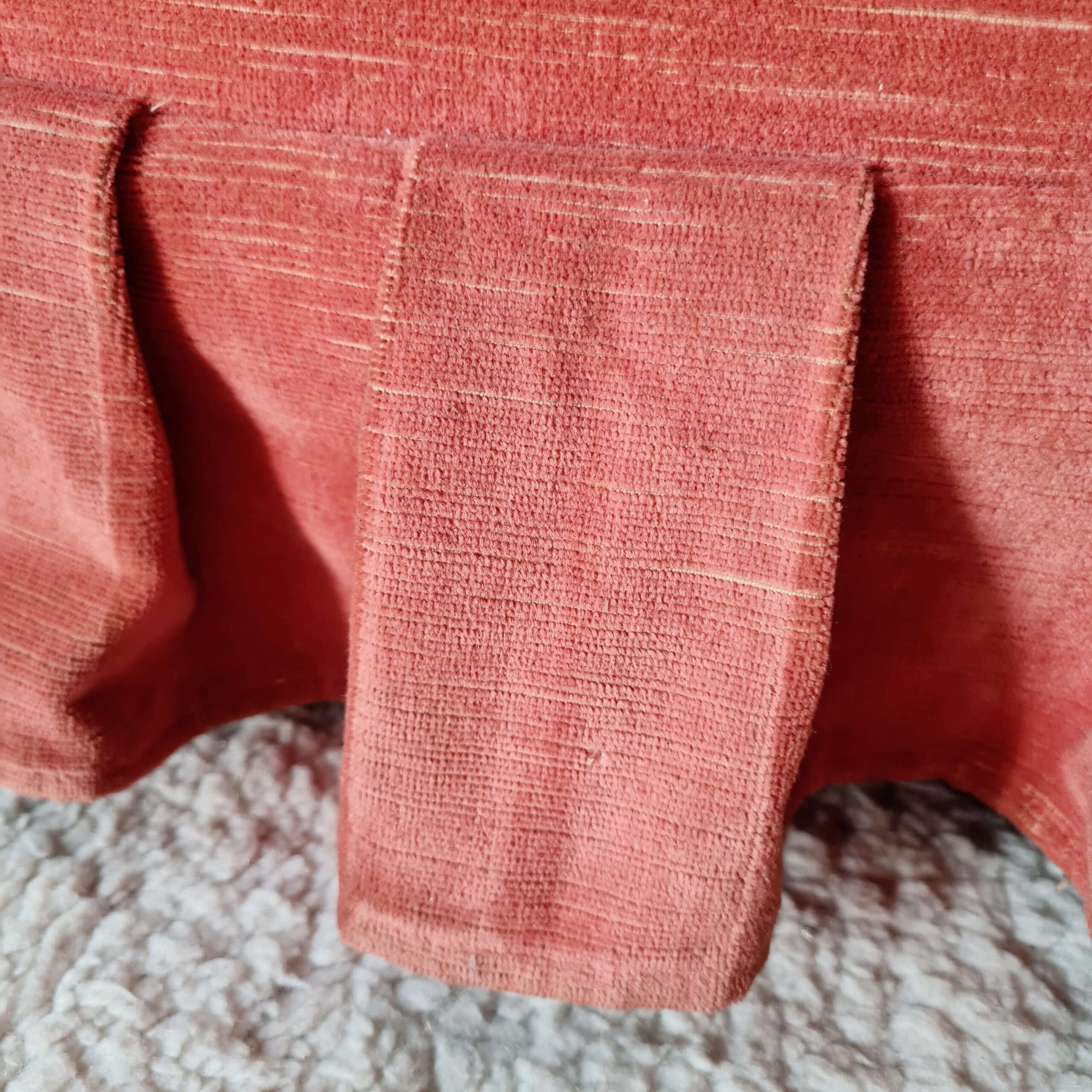 Gros plan sur les finitions et les plis de la jupe en tissu d'un fauteuil crapaud vintage.