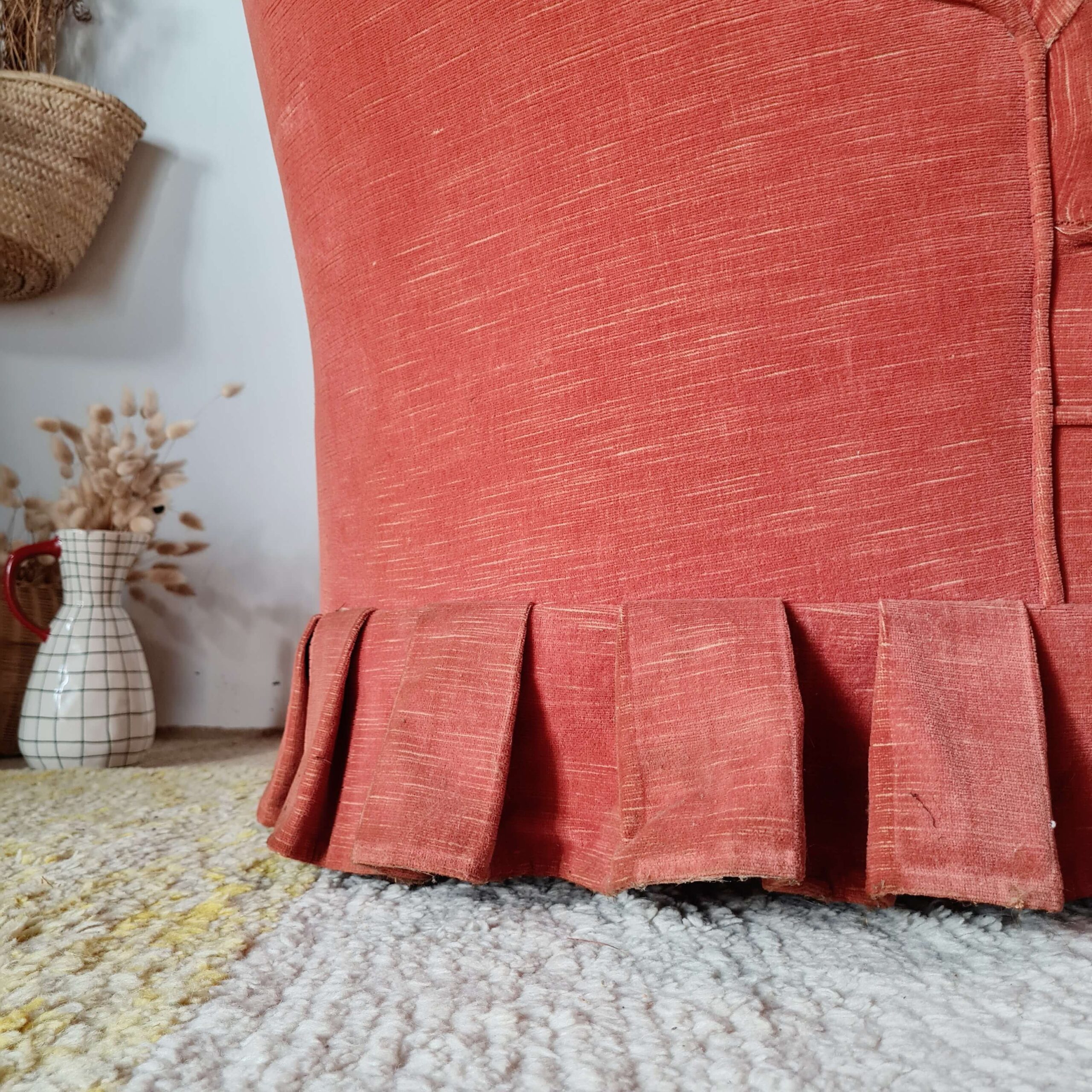 Gros plan sur les finitions de la jupe plissée en tissu d'un fauteuil vintage.
