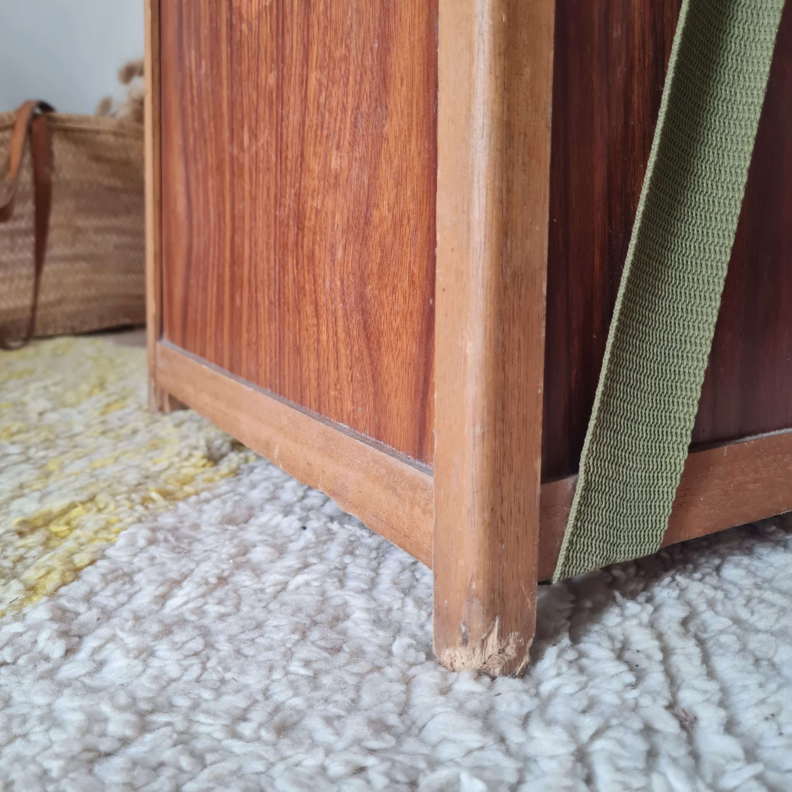 Très gros plan sur le bas d'un montant en bois et l'attache de la sangle verte du tabouret de pêcheur vintage.