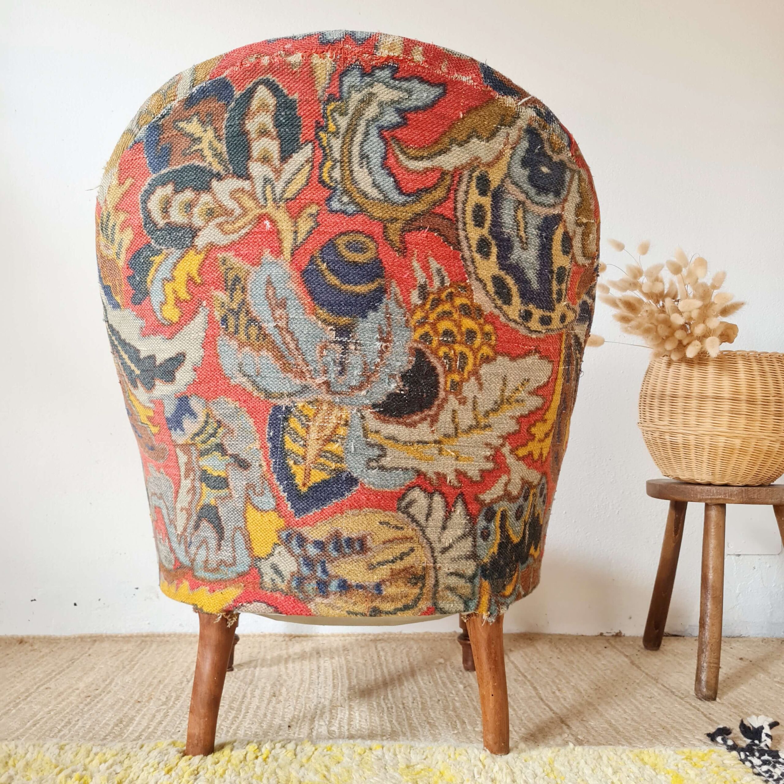 Vue arrière d'un fauteuil crapaud vintage dans une ambiance lumineuse, soulignant ses pieds en bois et son tissu à motifs tapisserie.