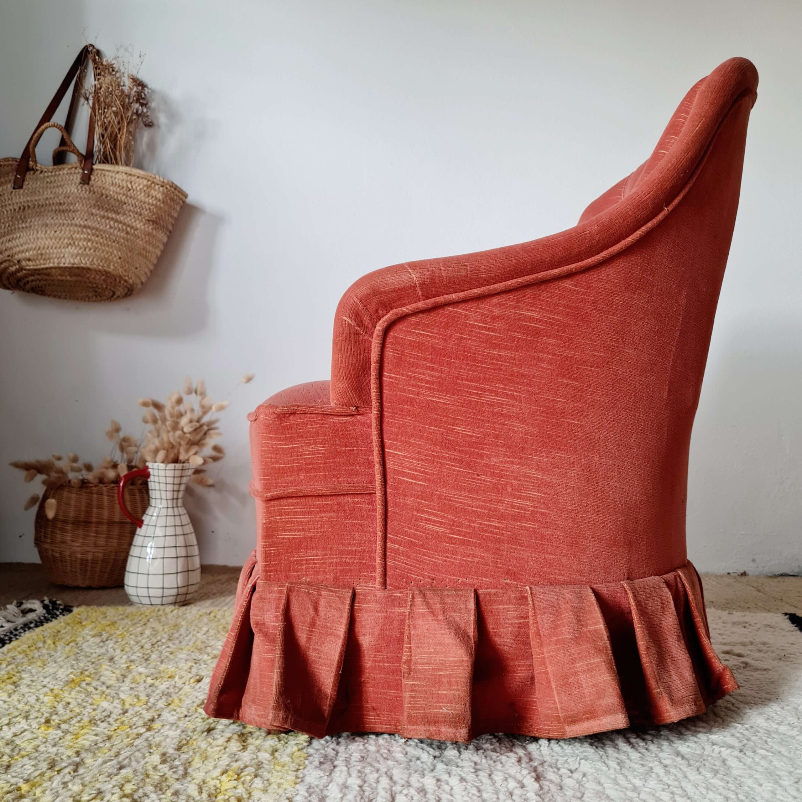 Vue de profil d'un fauteuil crapaud vintage rouge avec accoudoirs et jupe à volants plissés.