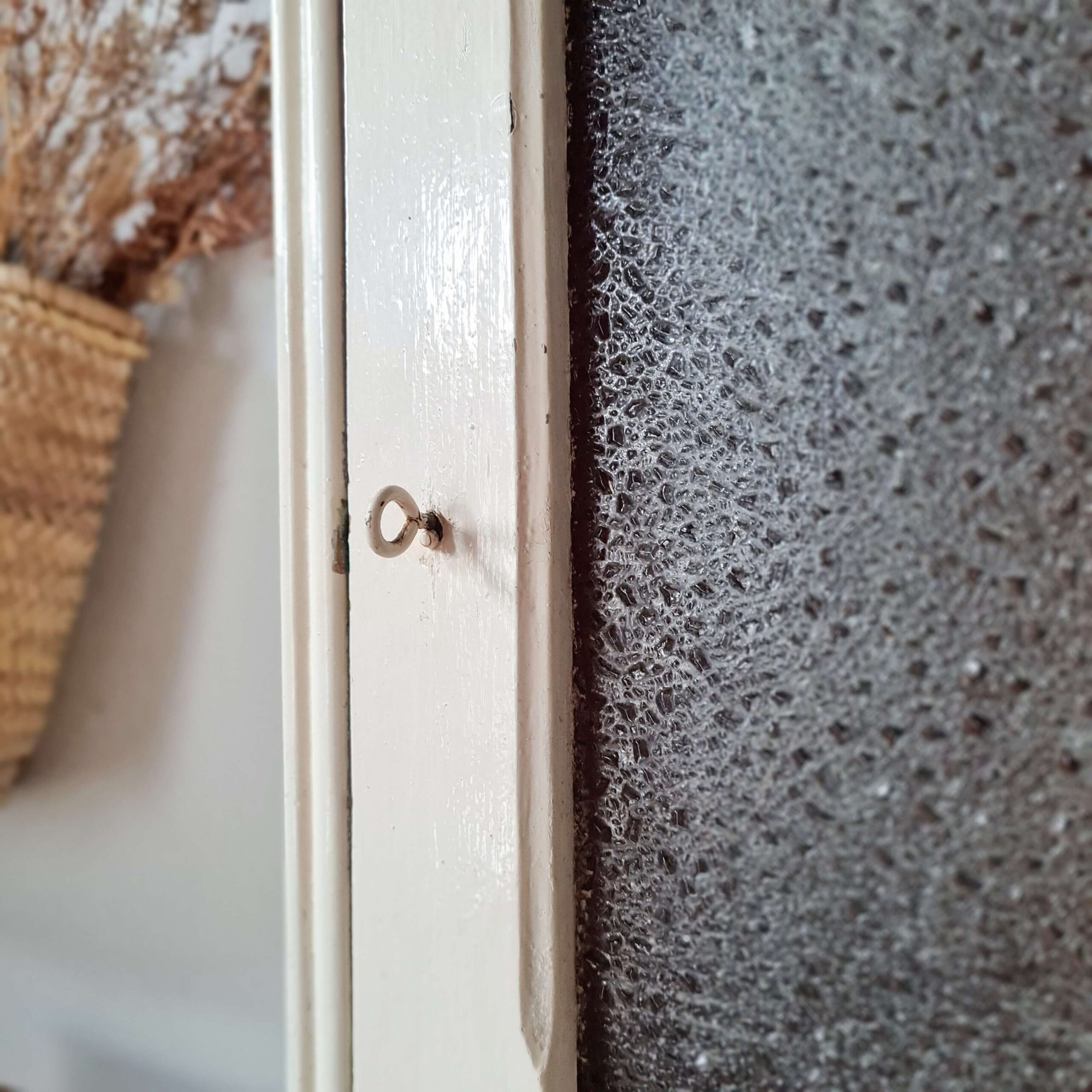 Gros plan sur le système de fermeture de la porte de la petite armoire vitrée, mettant en vedette le petit loquet métallique ancien fixé sur le montant en bois blanc.