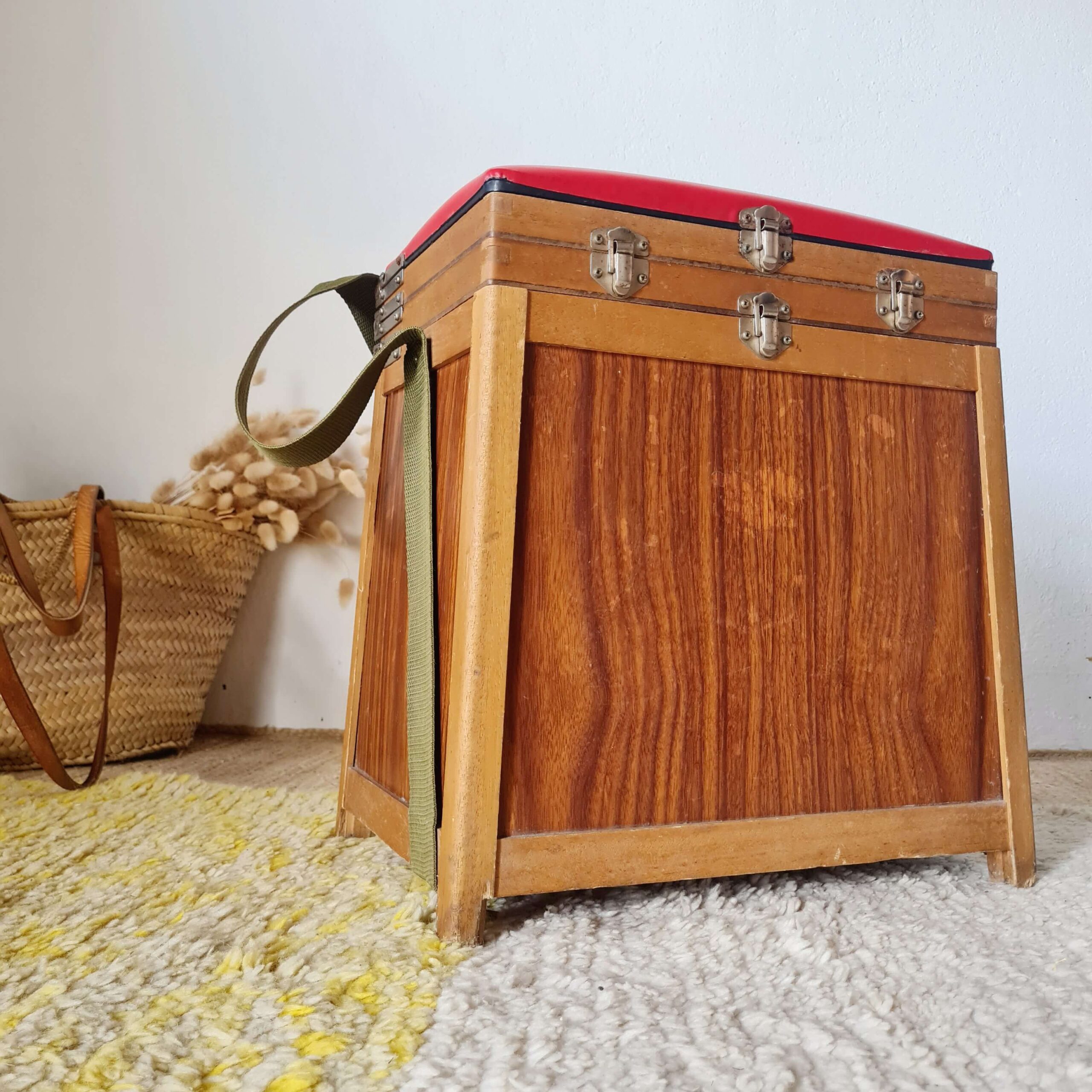 Vue de trois quarts de l'ancien tabouret de pêcheur avec son assise rouge, ses fermoirs et sa sangle de transport