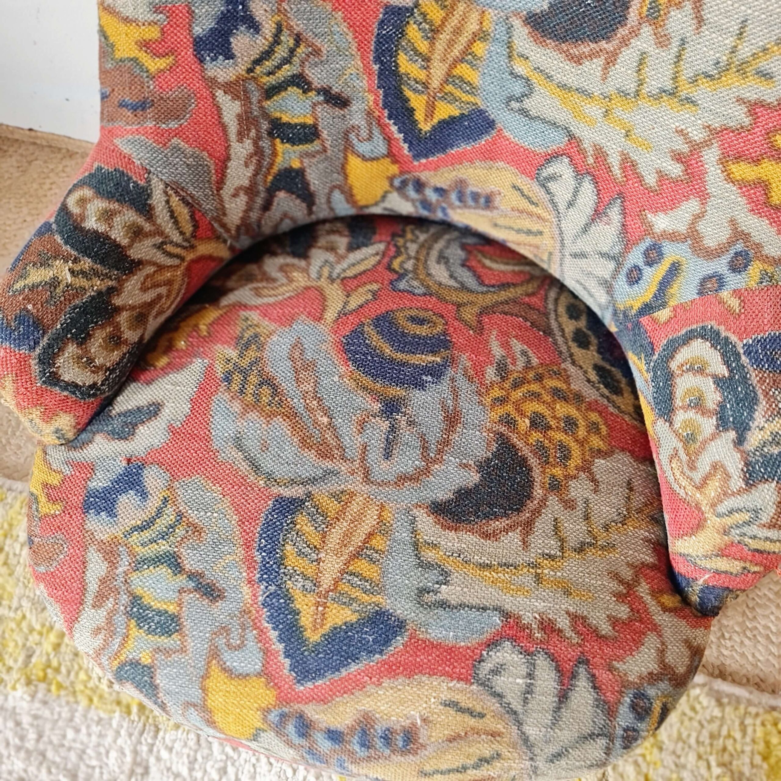 Vue du dessus de l'assise confortable d'un fauteuil crapaud vintage habillé d'un tissu fleuri aux teintes vibrantes.