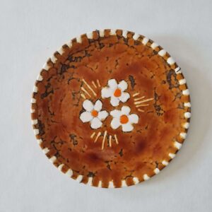 Assiette décorative vintage en céramique émaillée marron avec fleurs blanches et orange au centre.