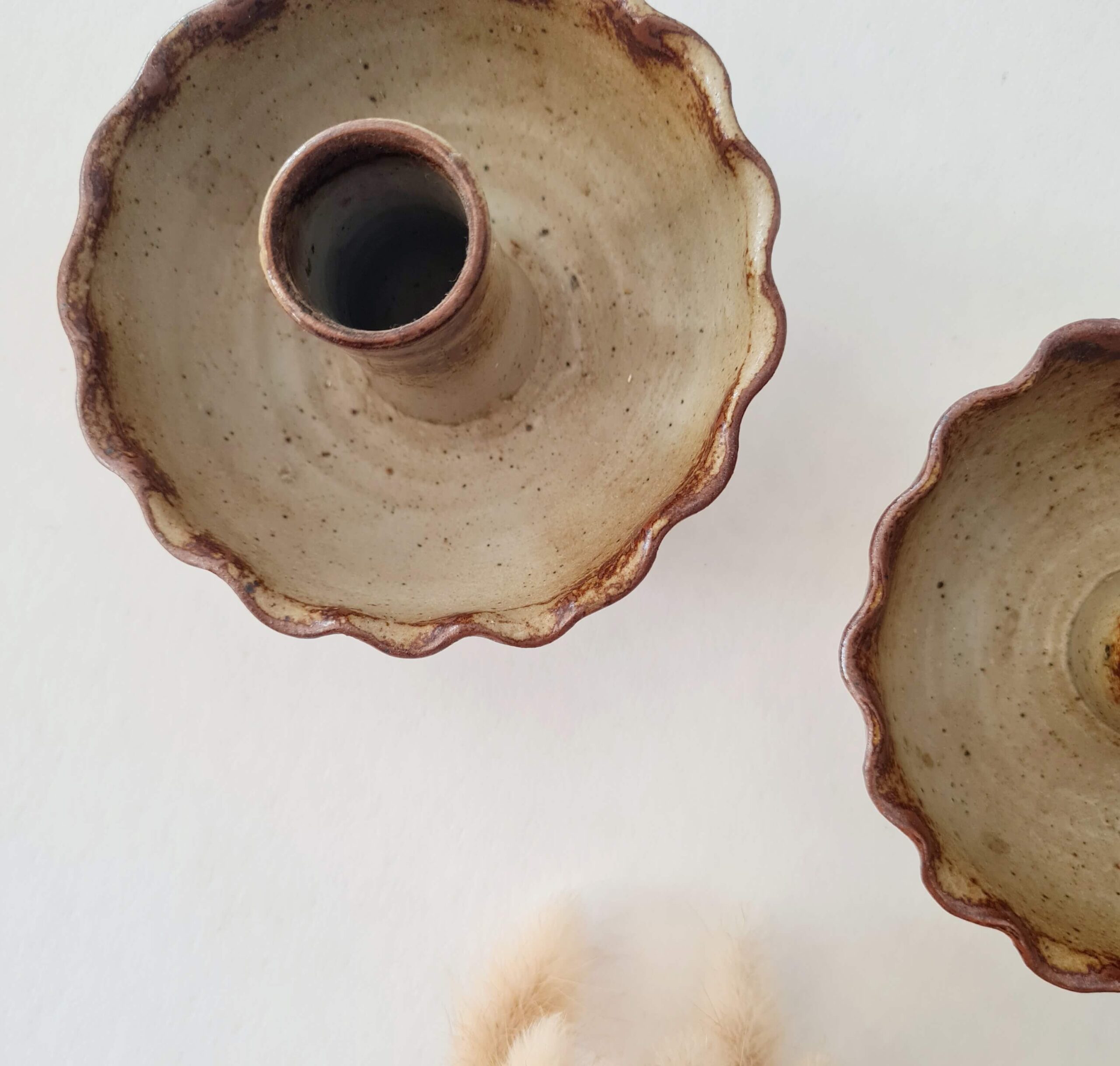 Vue de dessus d'une paire de bougeoirs anciens en grès moucheté accompagnés de fleurs séchées.