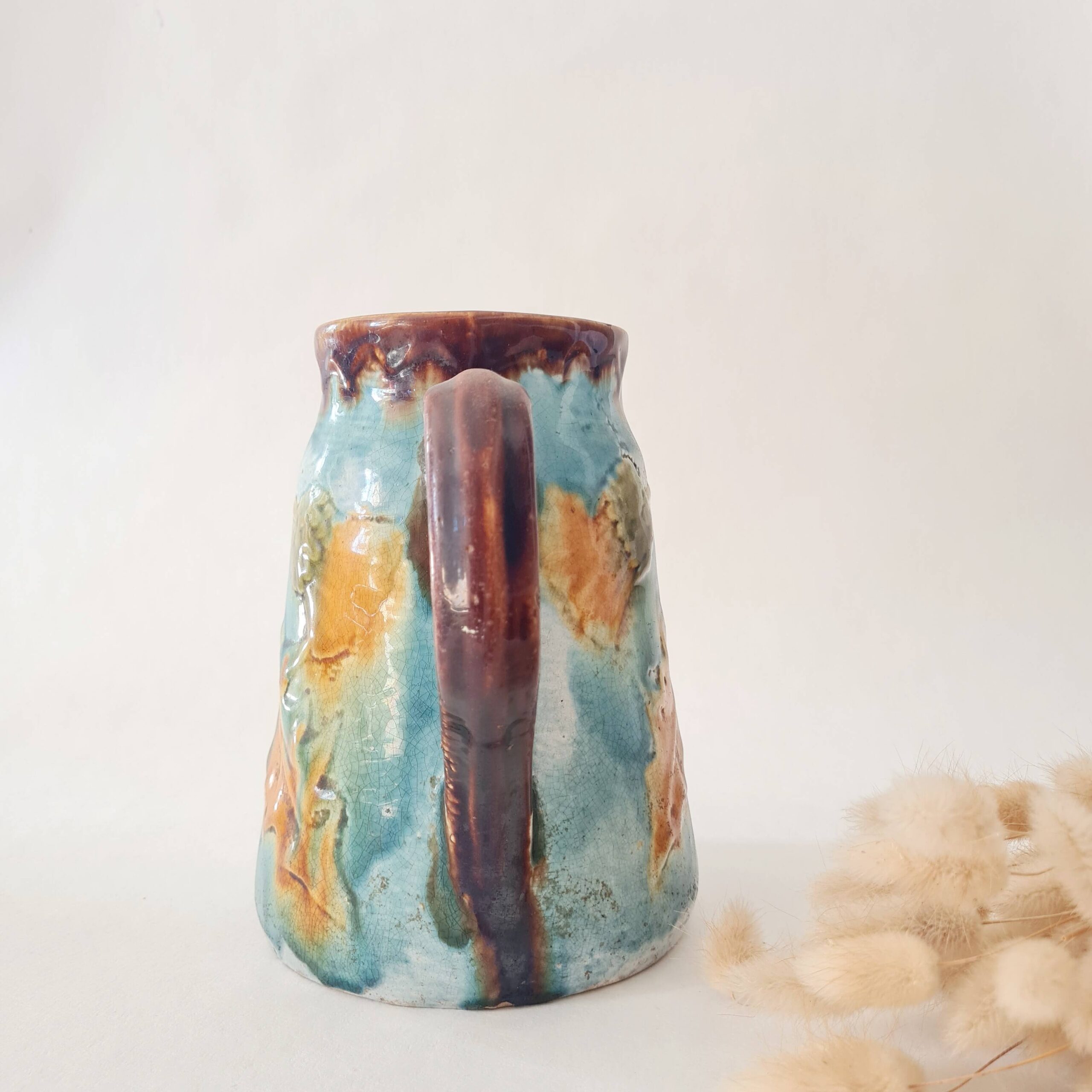 Pichet ancien en barbotine émaillée turquoise et marron avec motifs floraux en relief.