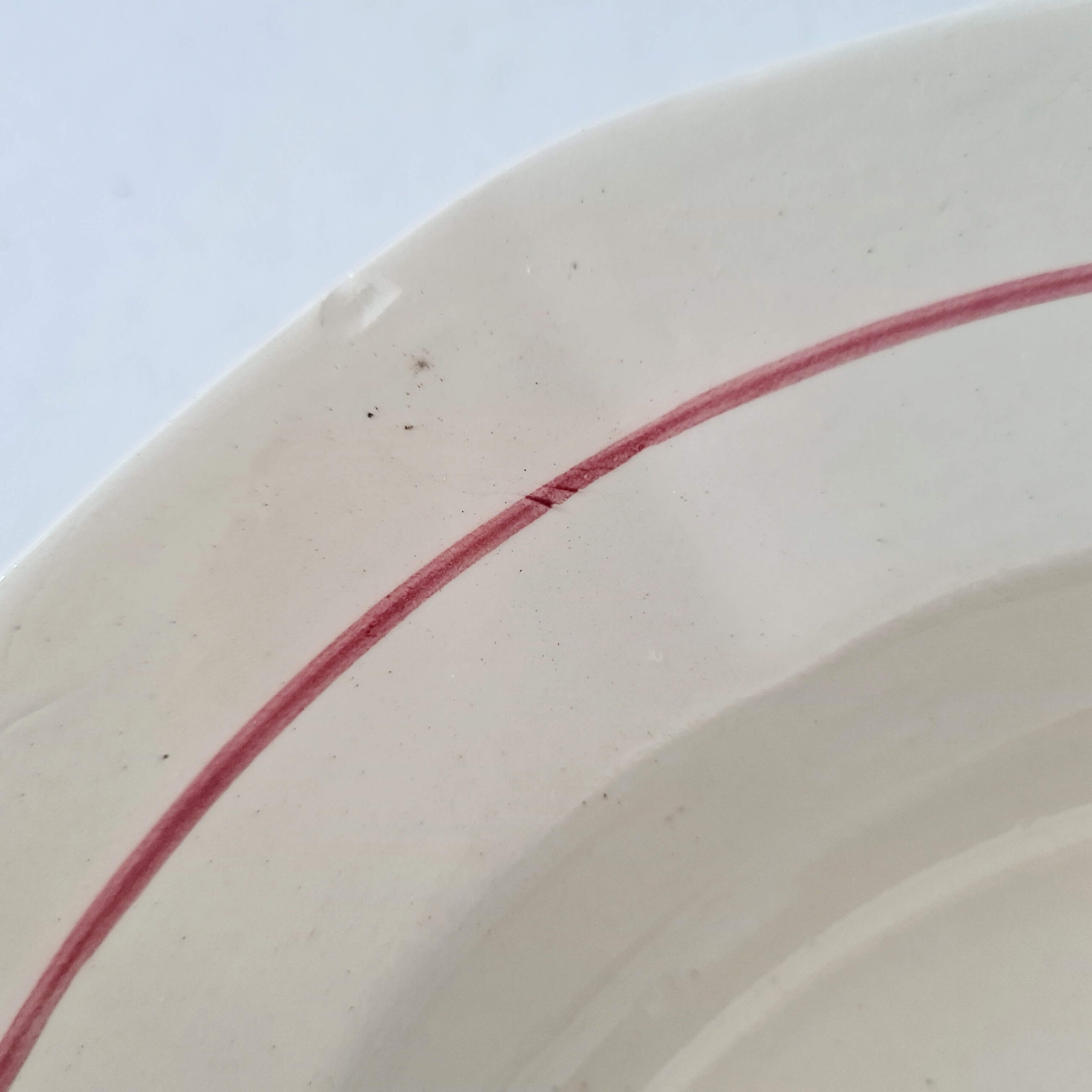 Détail du marli et du liseré bordeaux sur l'assiette en faïence ancienne