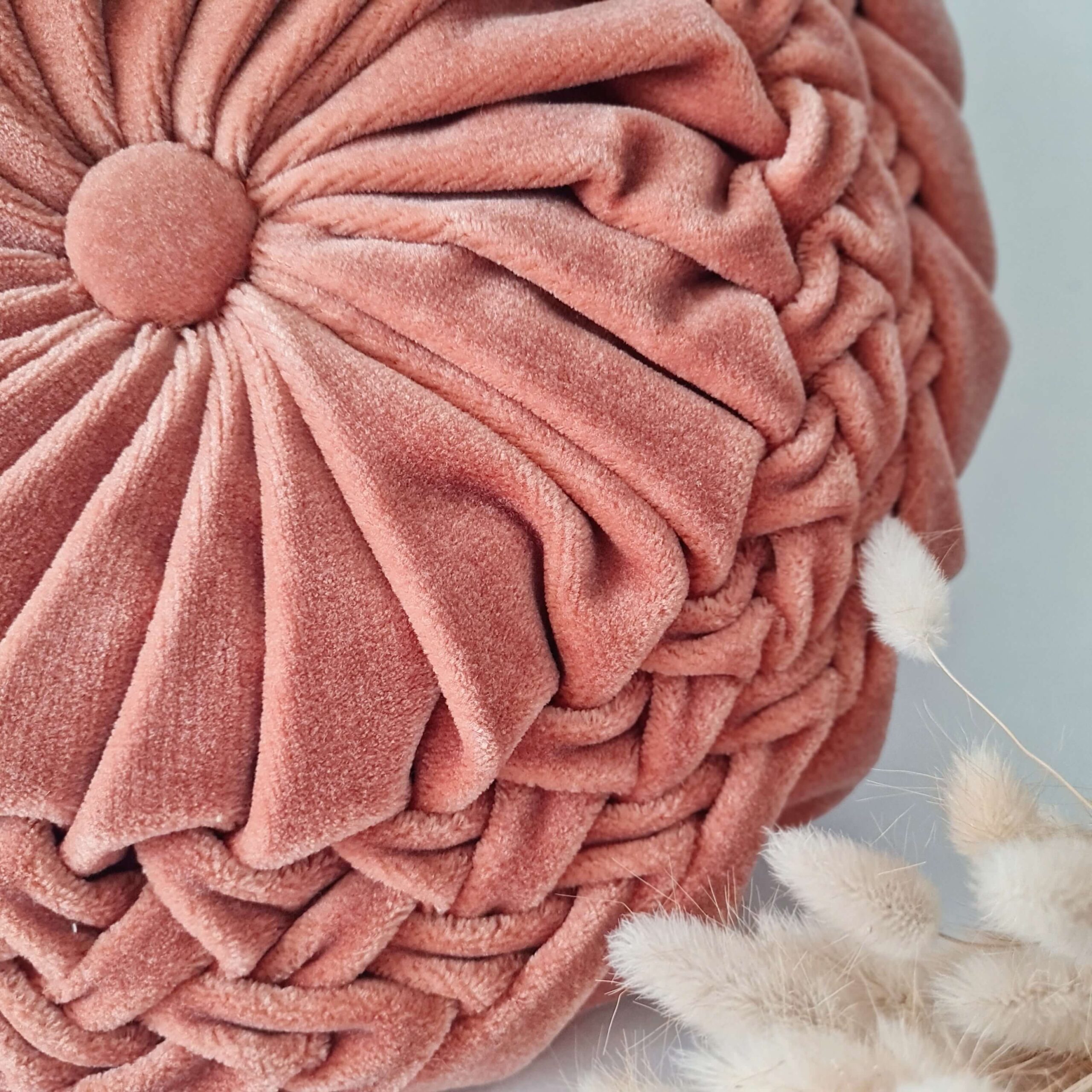 Gros plan sur le plissé en rosace et le bouton central du coussin rond en velours