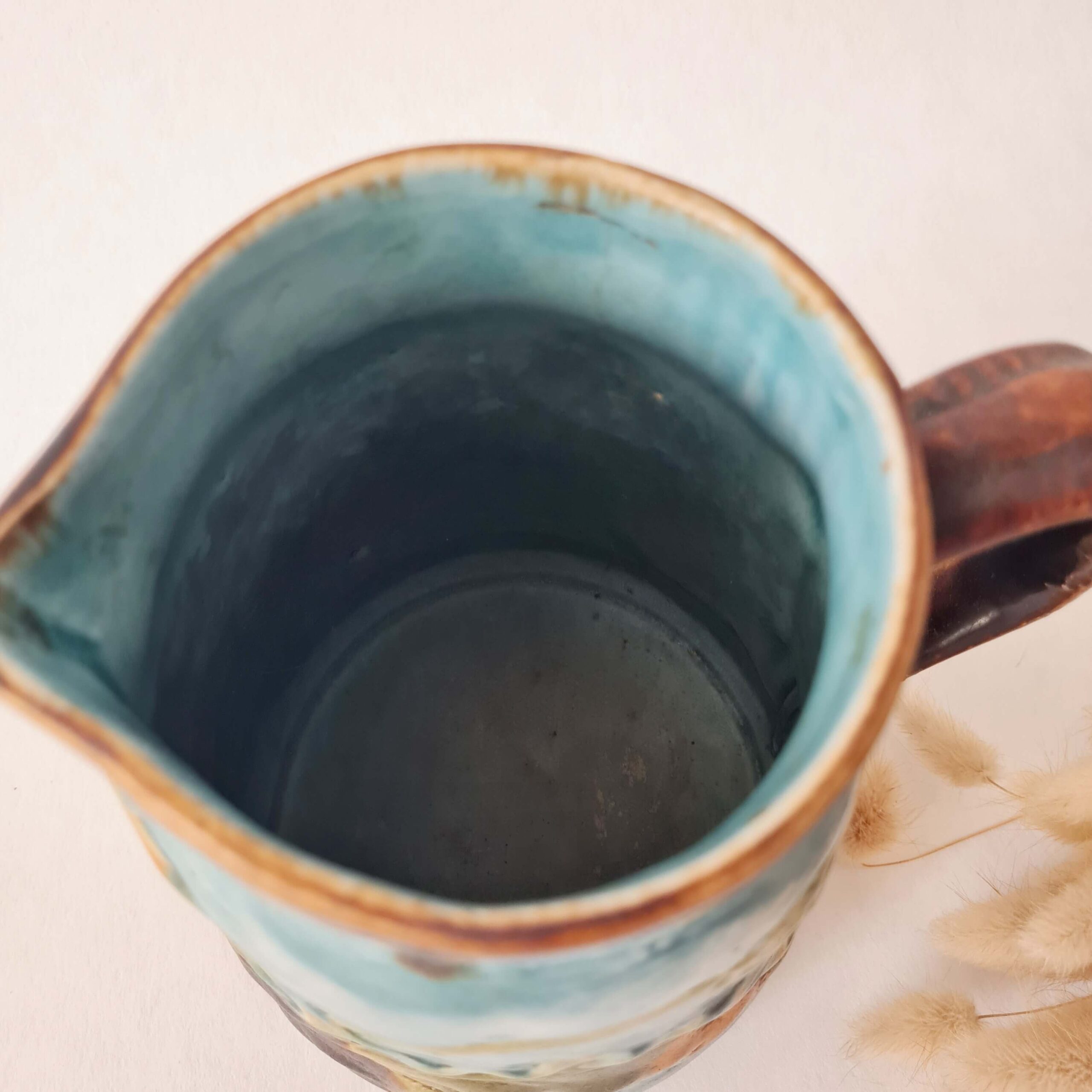 Vue plongeante de l'intérieur émaillé bleu turquoise d'un pichet en barbotine.