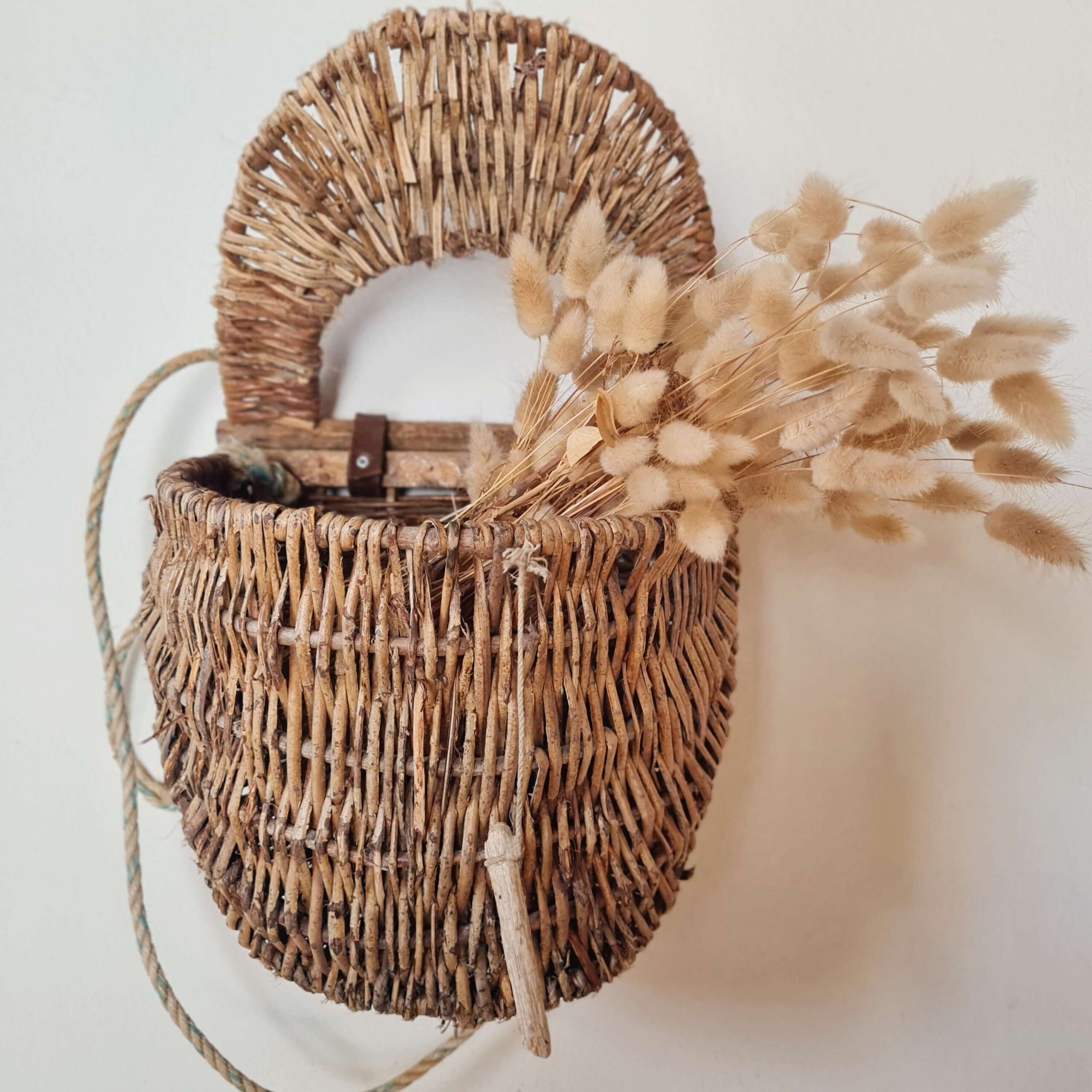 Panier en osier suspendu au mur décoré d'un bouquet de fleurs séchées.