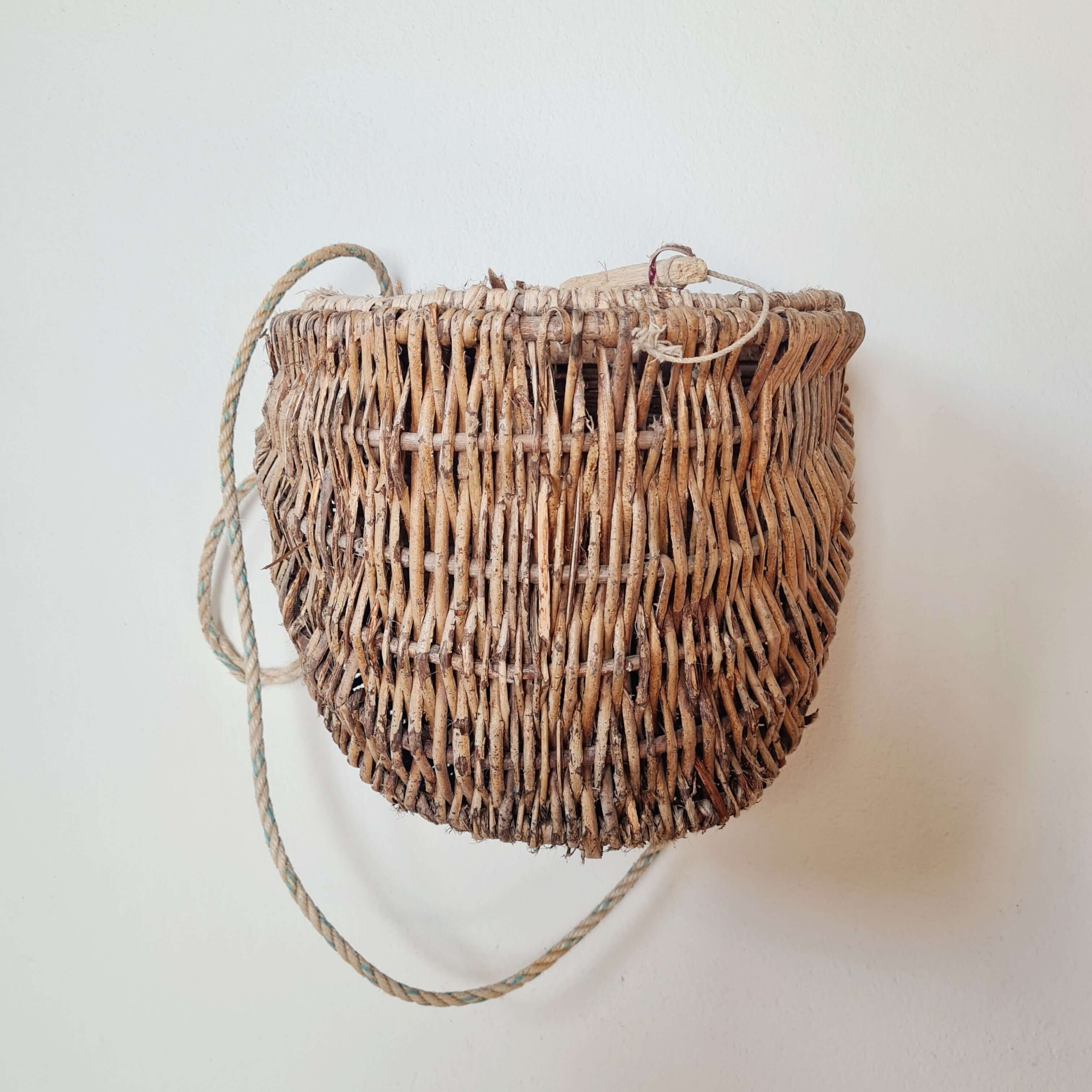 Panier suspendu mural ancien en osier tressé brut avec corde d'accroche.