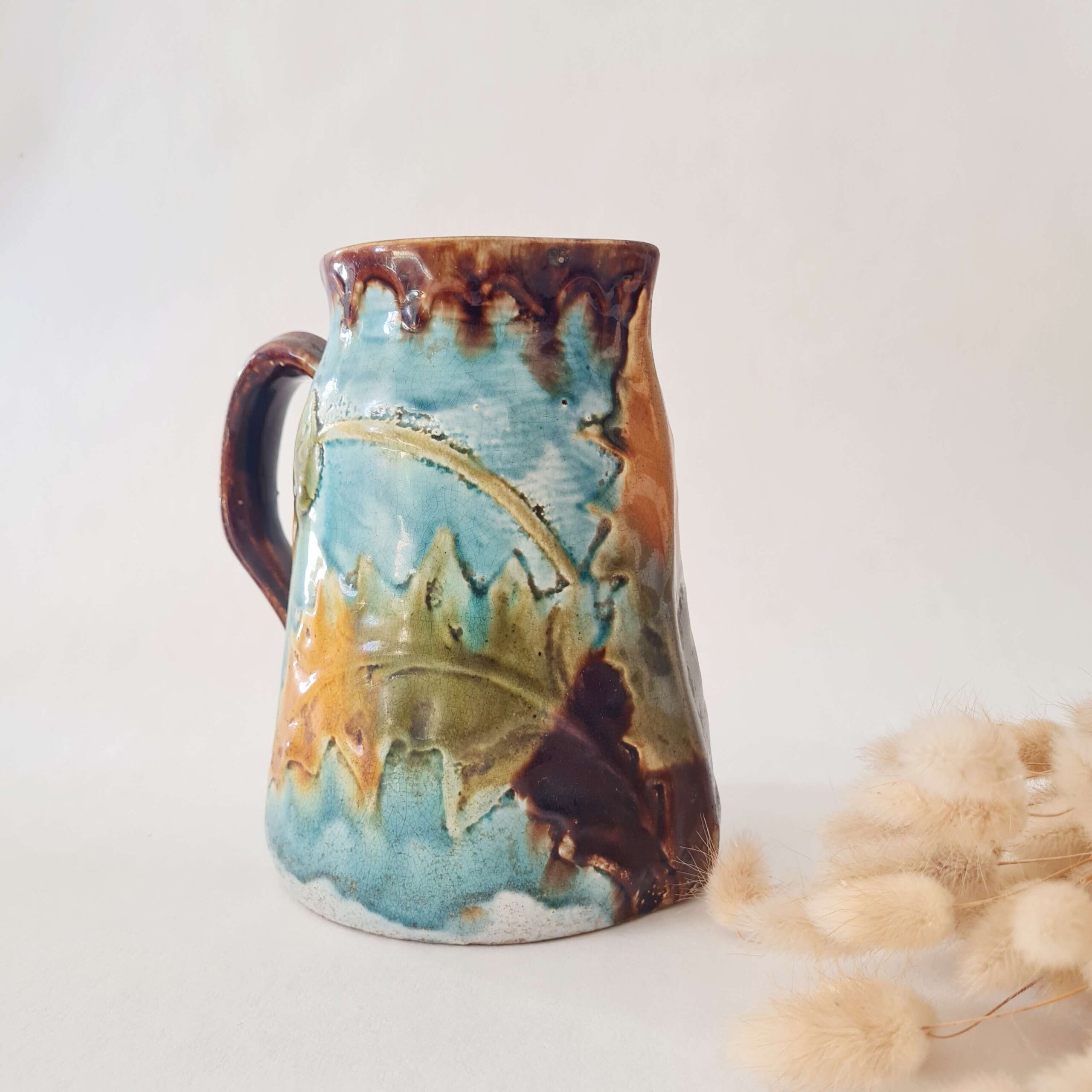 Pichet ancien en barbotine émaillée turquoise et marron avec motifs floraux en relief.