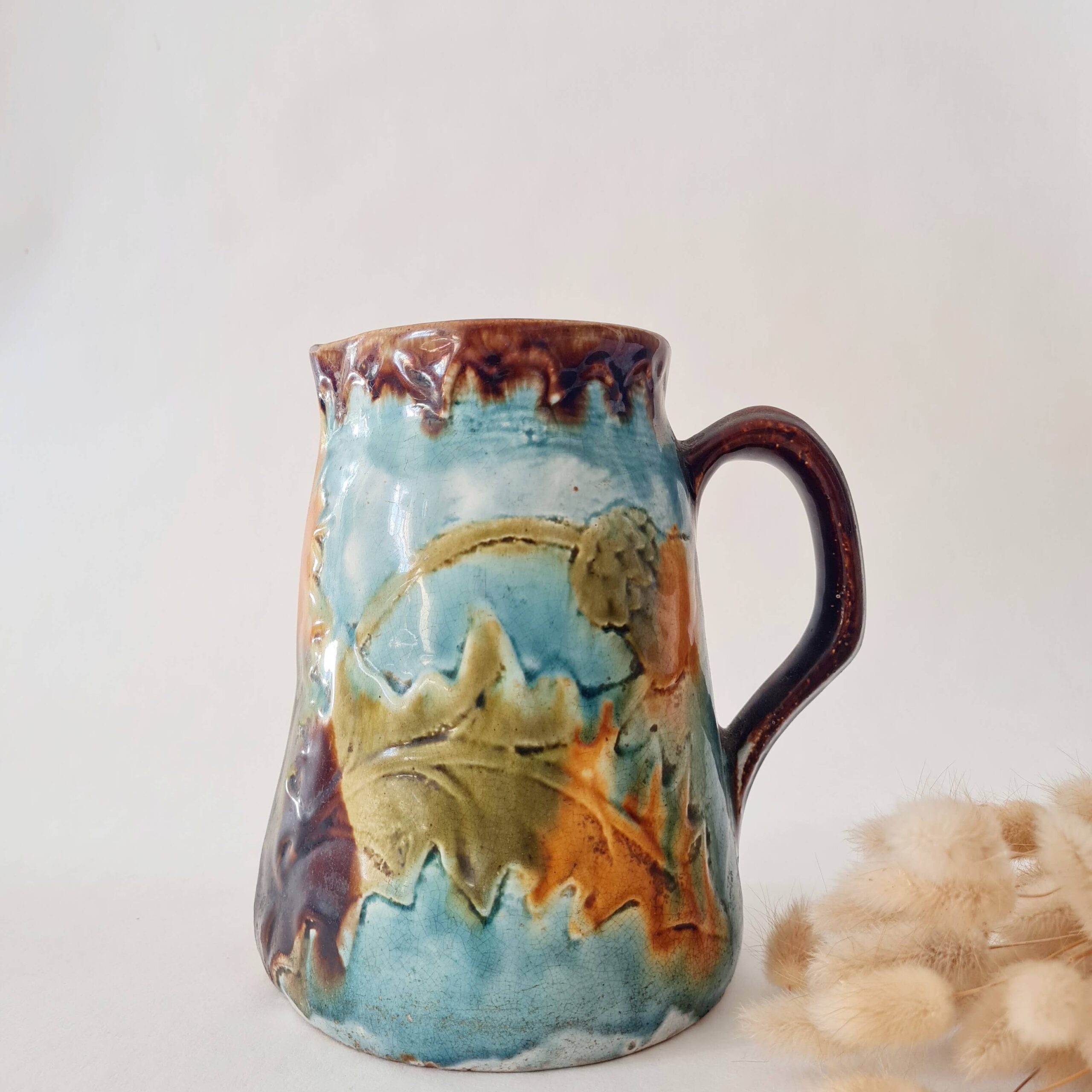 Cruche en céramique barbotine d'époque Art Nouveau avec anse et décors végétaux.