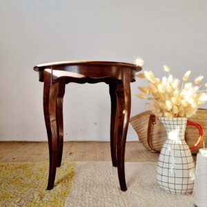 Table d'appoint vintage ronde en bois sombre prise de profil éclairée par la lumière naturelle.